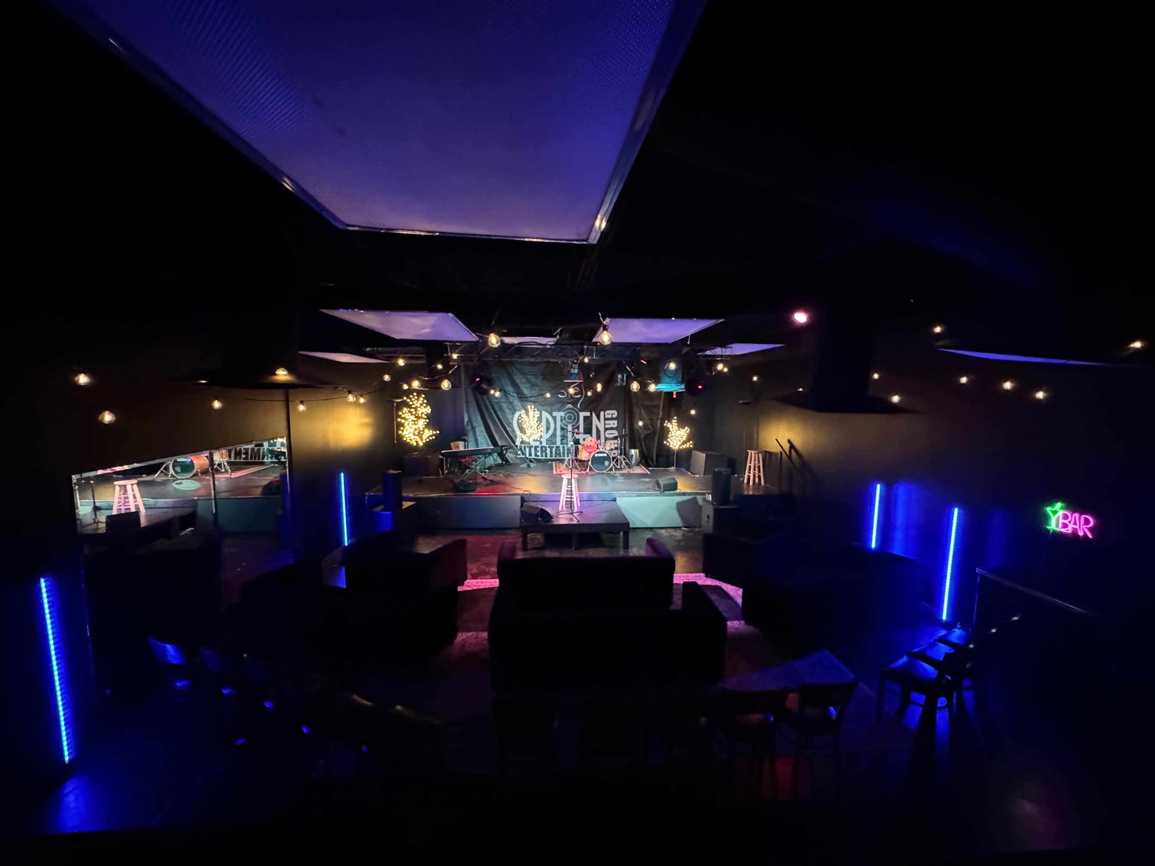 A dimly lit performance venue featuring a stage with instruments, scattered seating areas, and decorative lights.