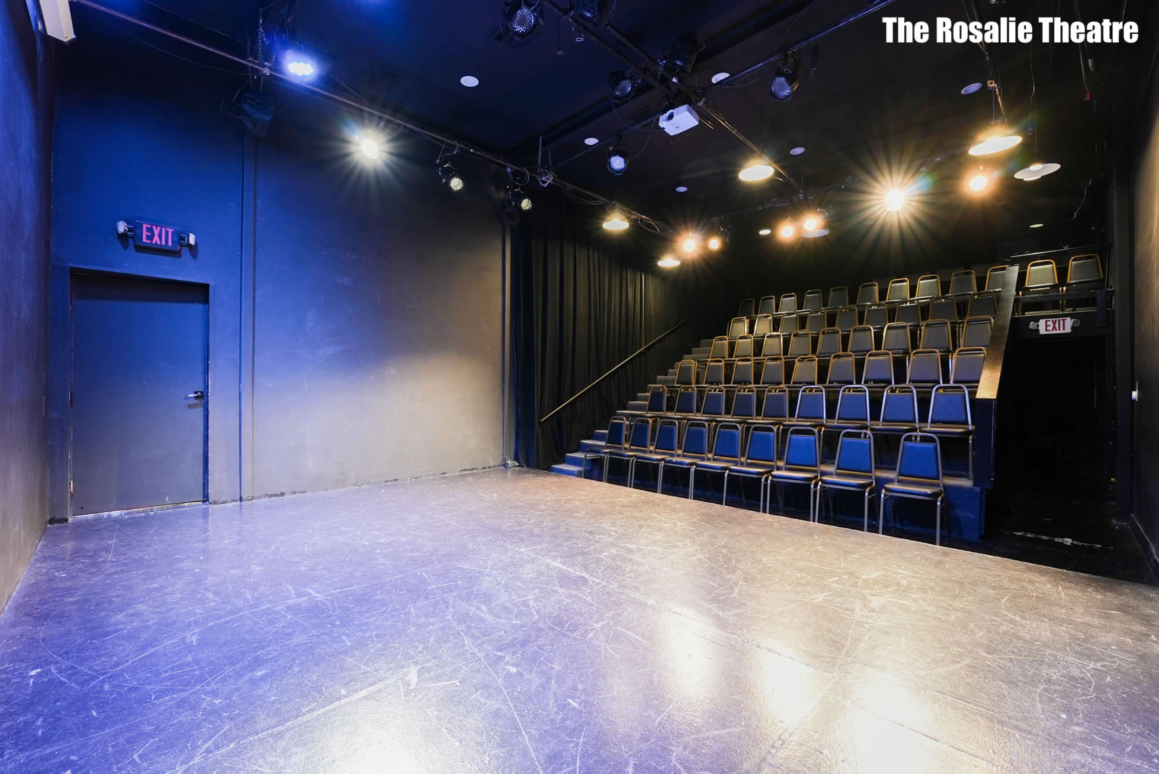 The image shows a dark theater stage with a set of empty seats arranged in a semi-circular format in the background.