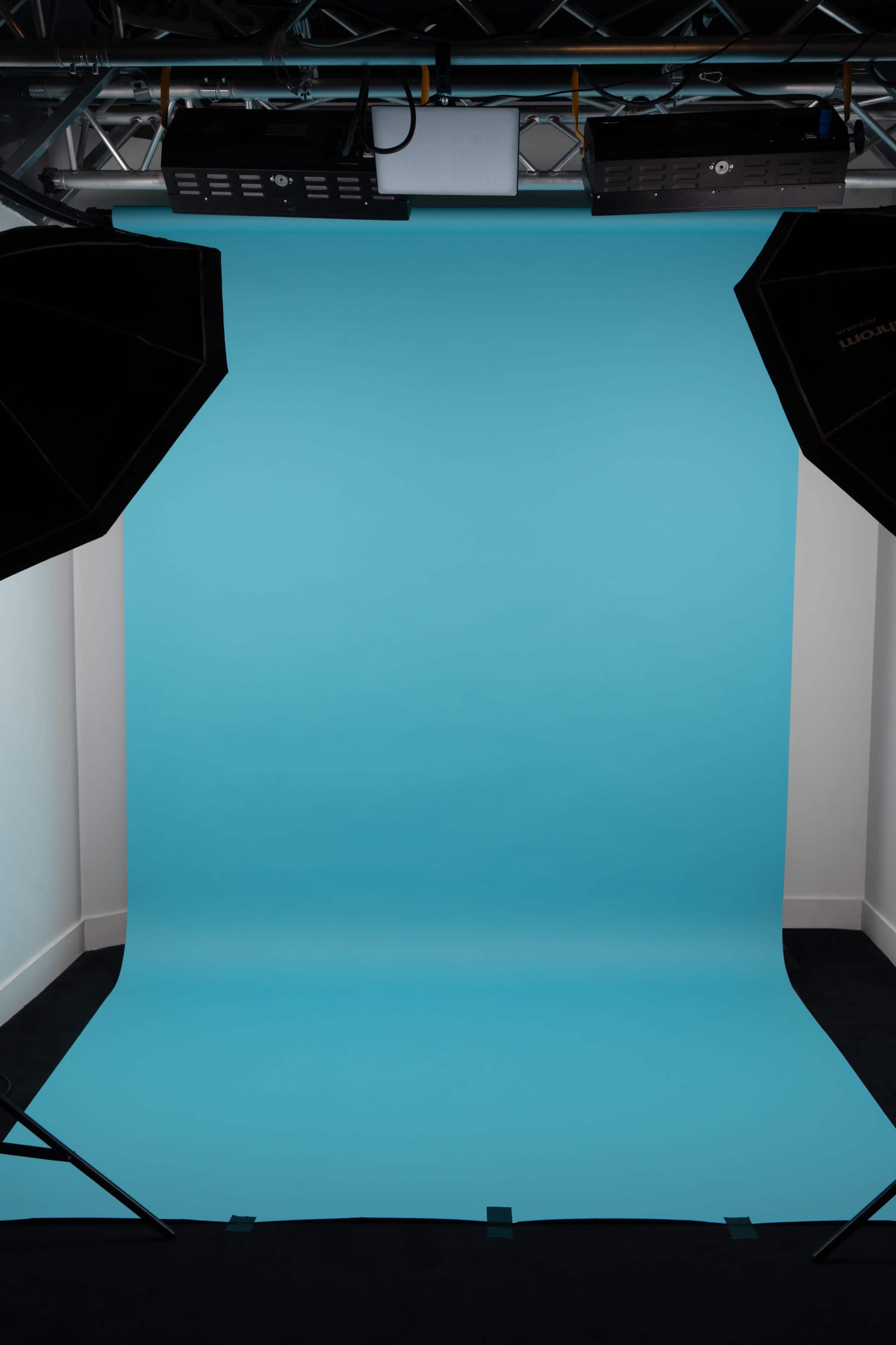 A photo studio is set up with a solid light blue backdrop and two black softbox lights positioned on either side.