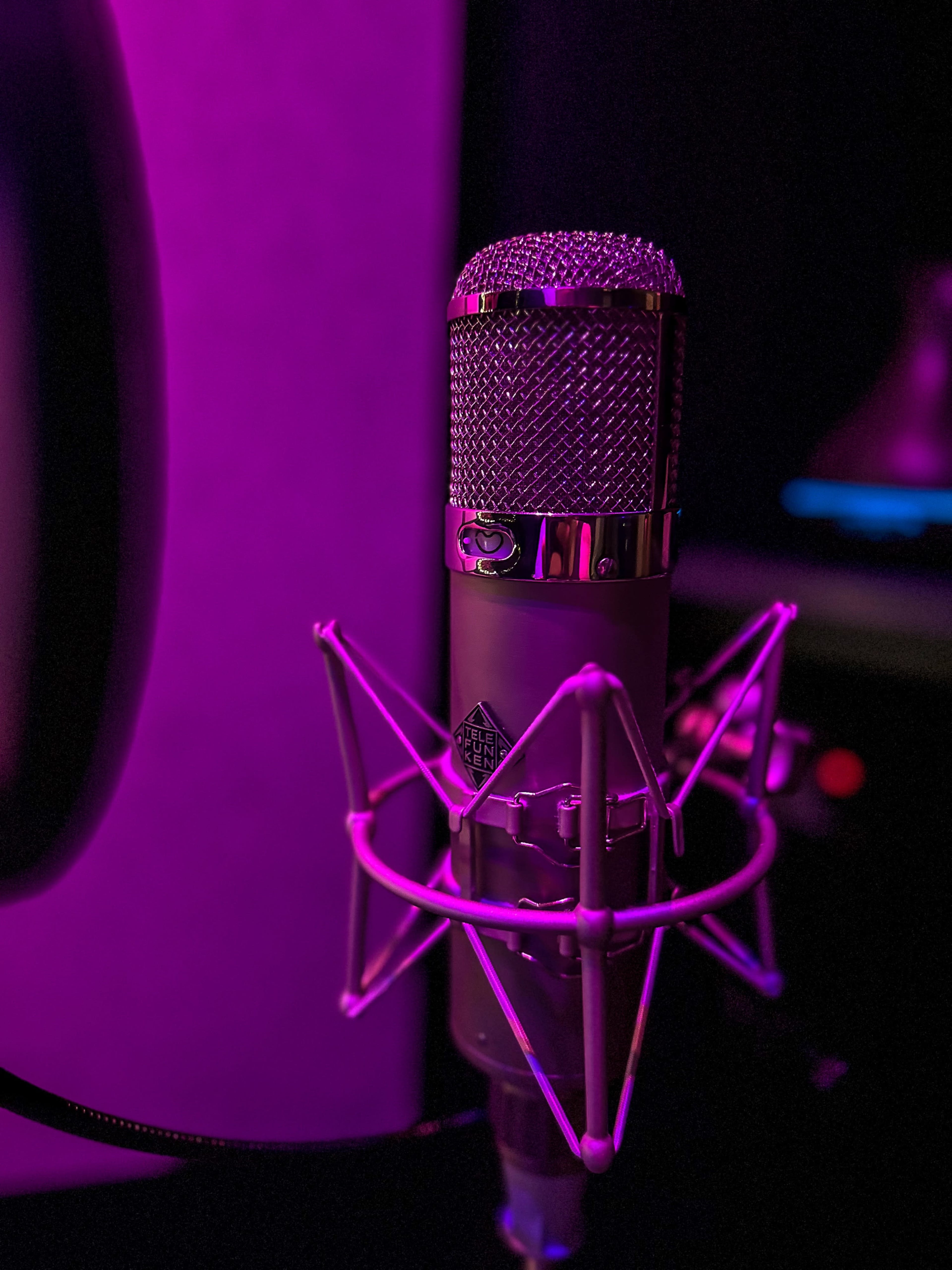 A close-up of a microphone with a pop filter, set against a dark background illuminated by purple light.