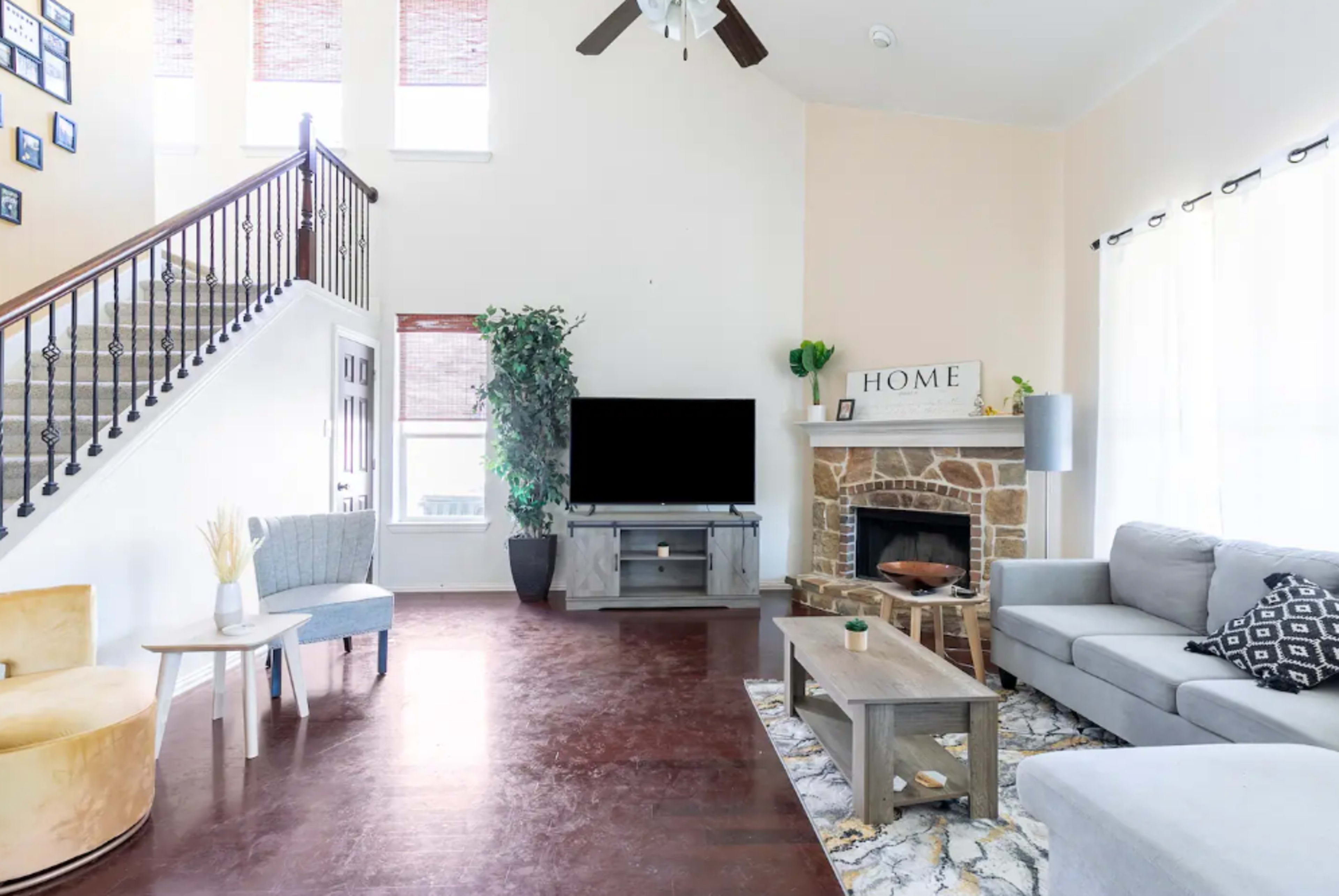 A spacious living room featuring a stone fireplace, modern furniture, and a large television mounted on a wall.