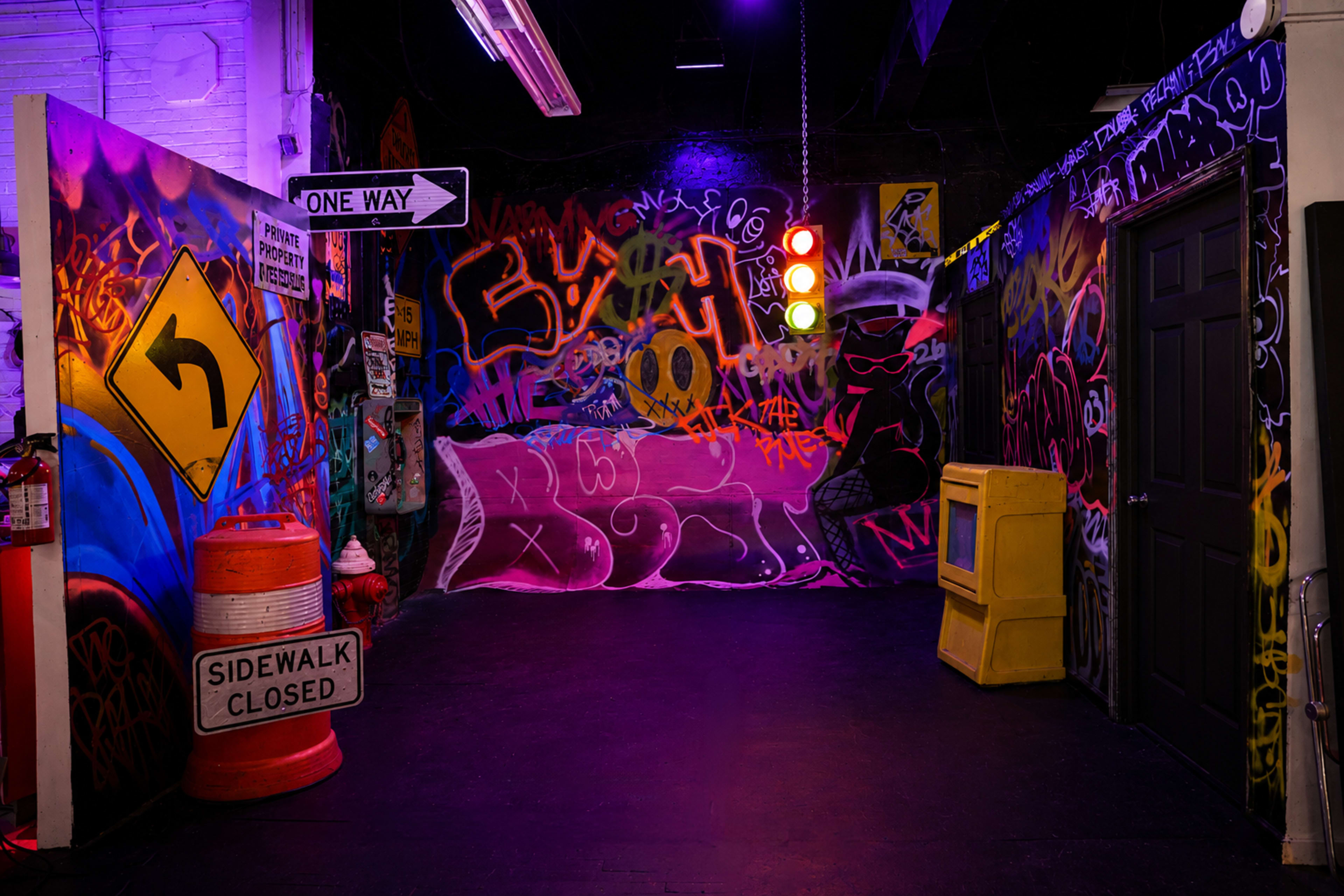 The image depicts a colorful, graffiti-covered room with street signs, a traffic light, and various objects like a yellow television and a traffic cone.