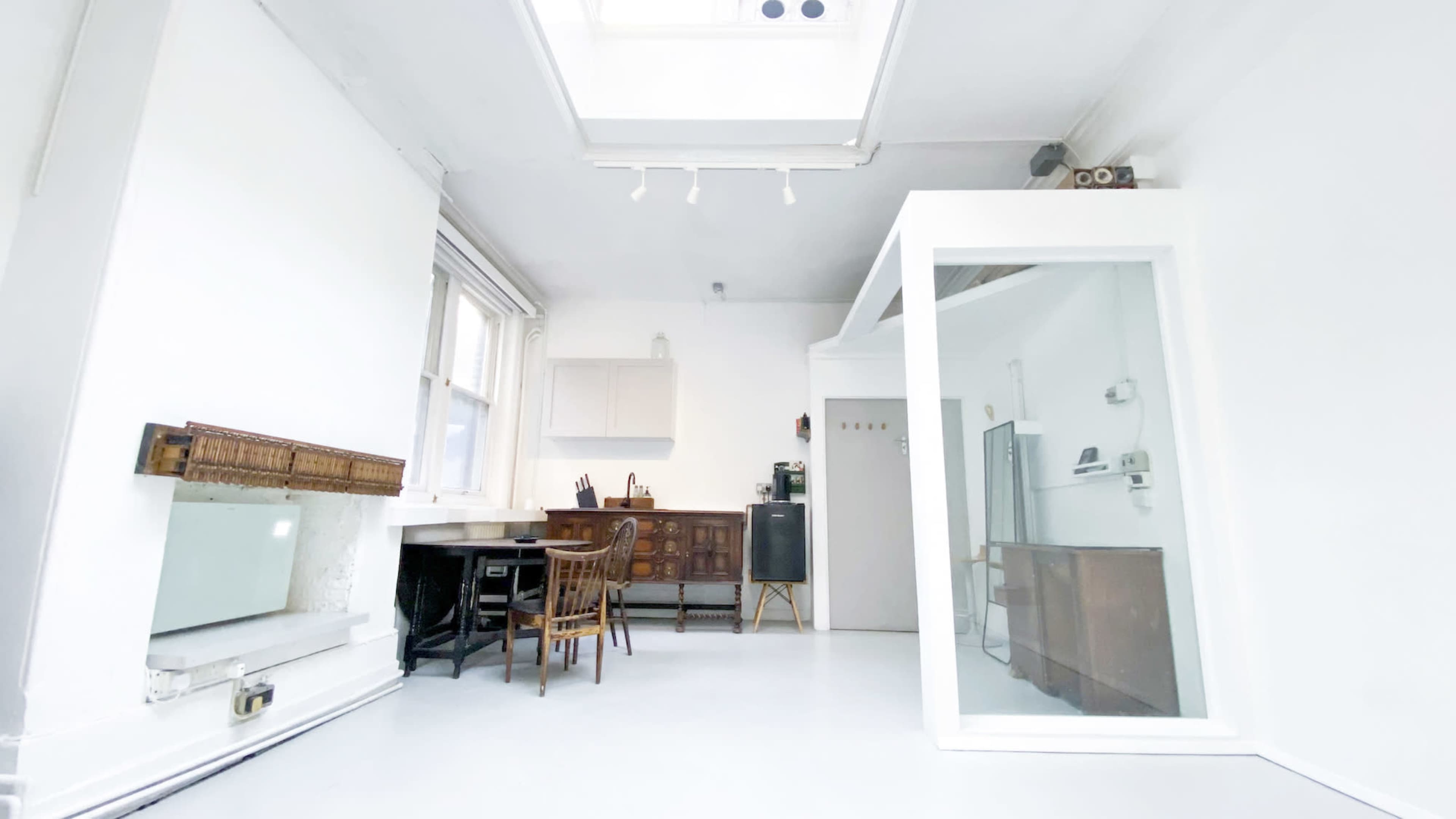 A bright, minimalistic room with white walls, a skylight, and wooden furniture including a table and chairs.