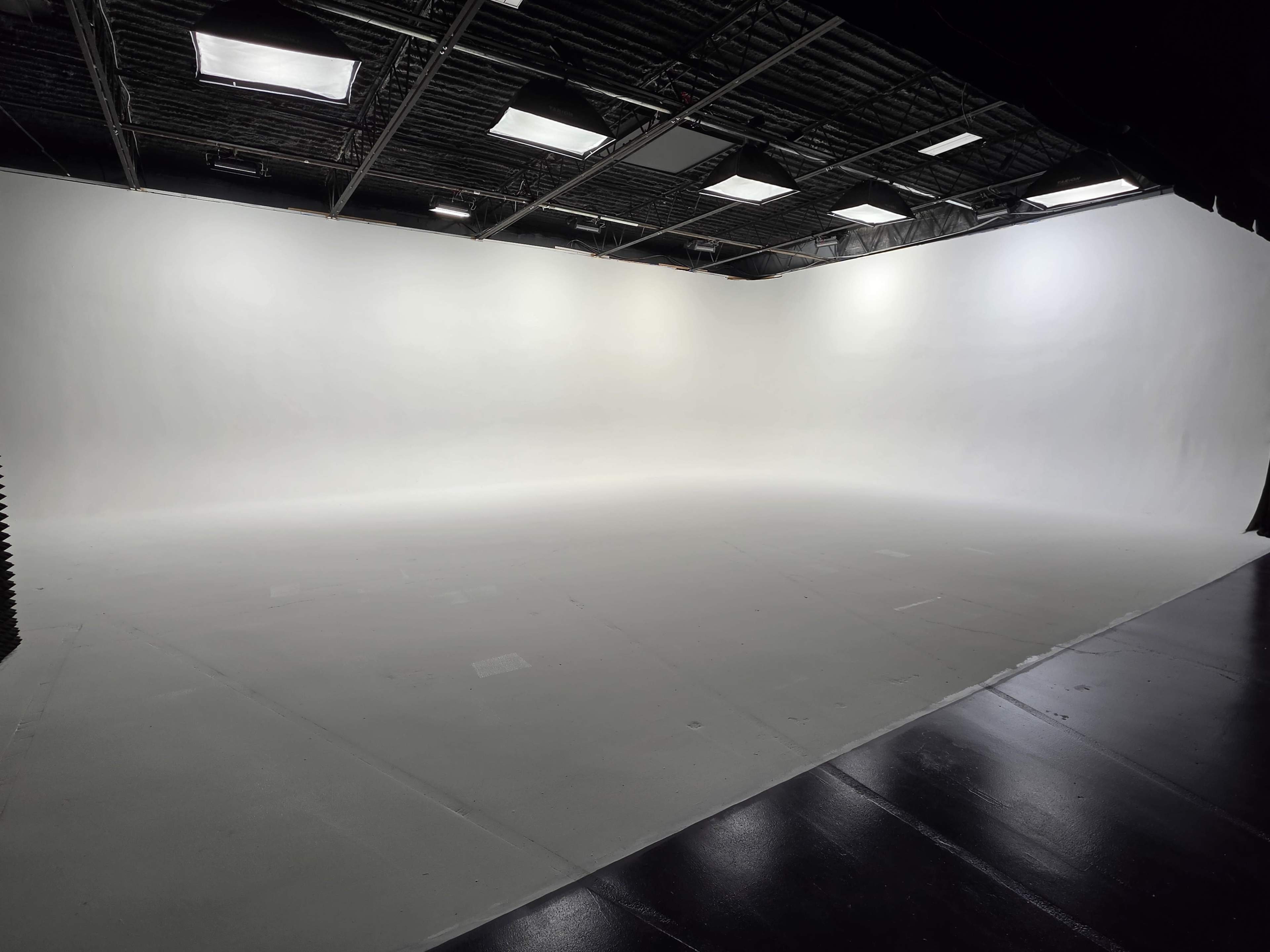 The image shows a spacious, empty studio with a plain white backdrop and overhead lighting.