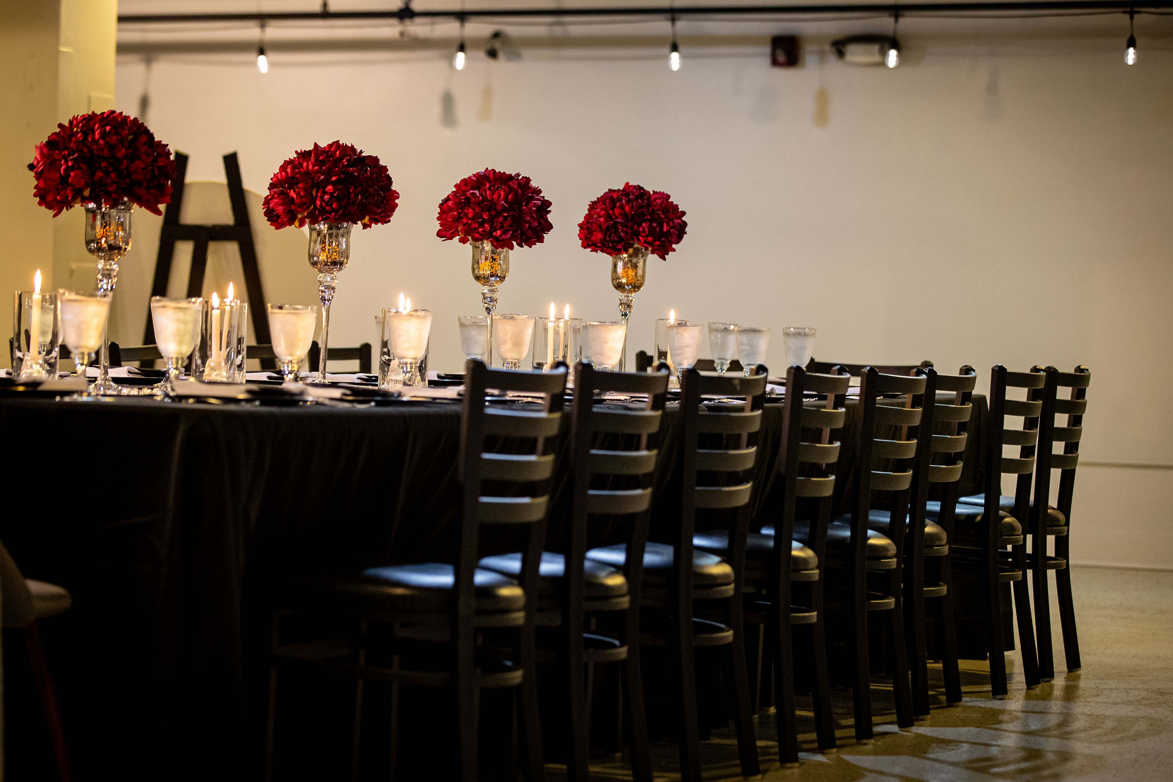 A long dining table is set with elegant glassware, floral arrangements, and candles, surrounded by black chairs.