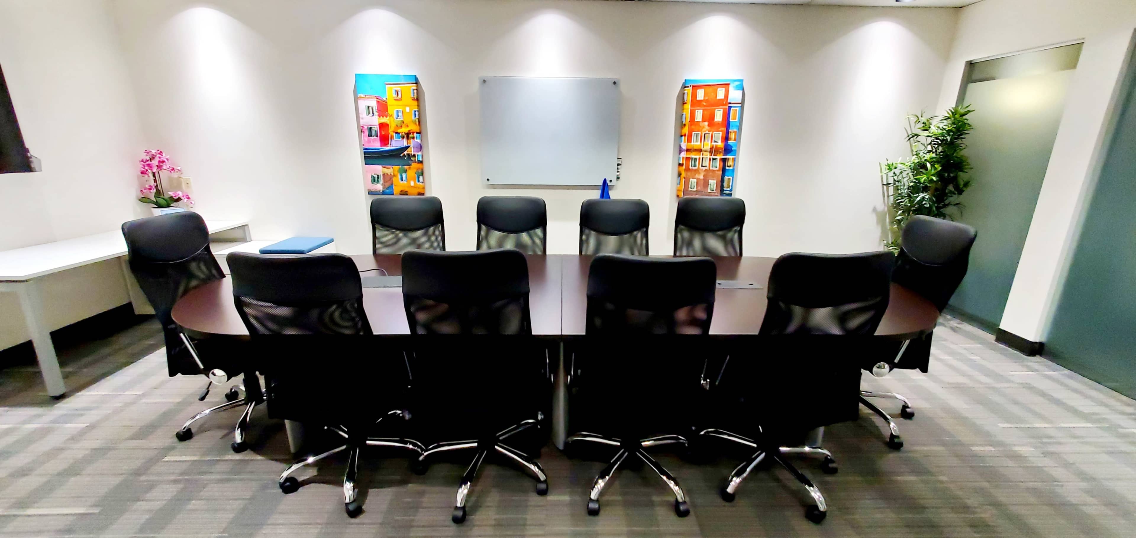 A large conference room features a rounded table surrounded by black chairs, with colorful artwork on the walls and a whiteboard at the front.
