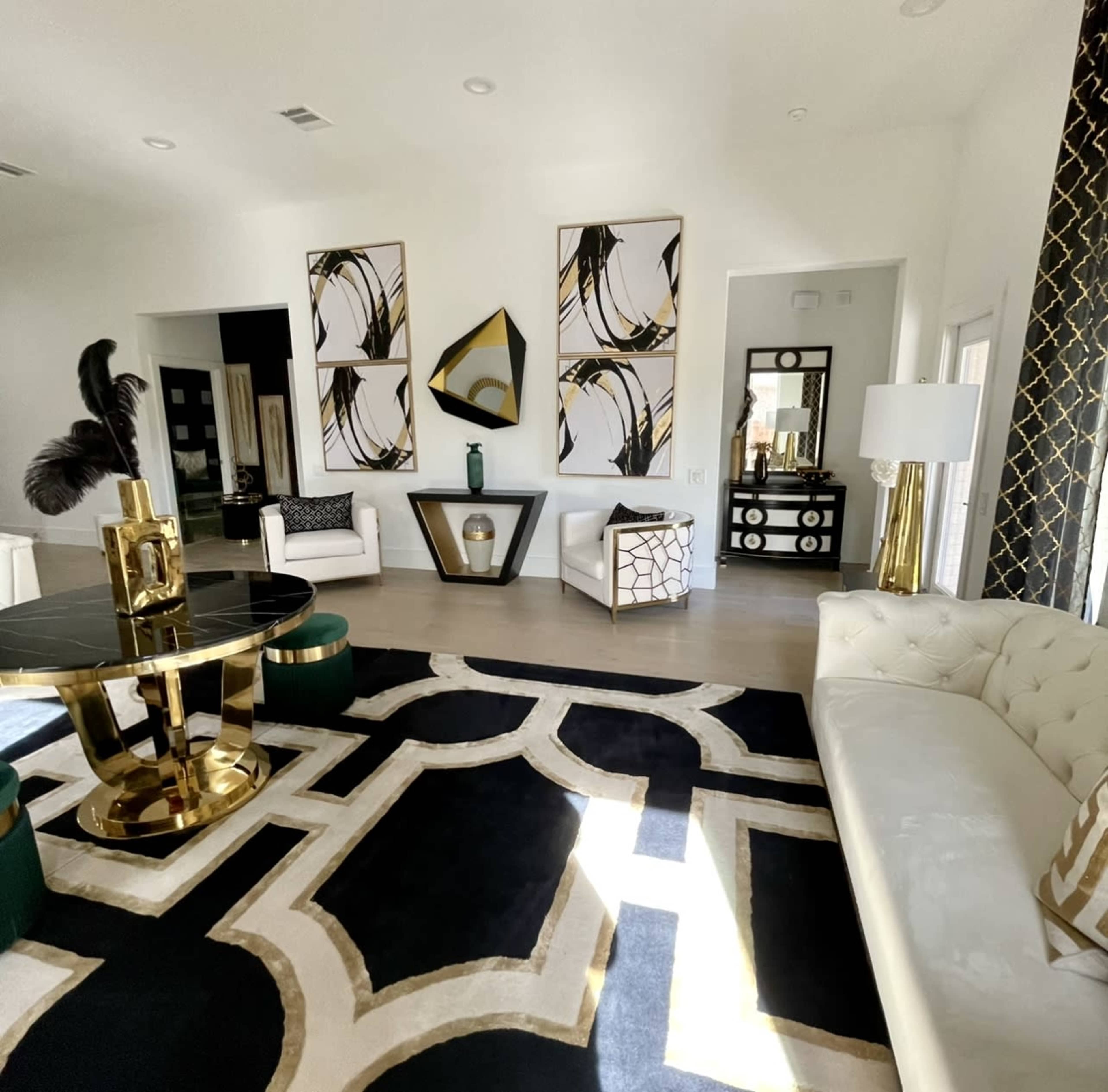 The living room features modern decor with a black and gold color scheme, including a large area rug, a glass and metal coffee table, and two white armchairs.