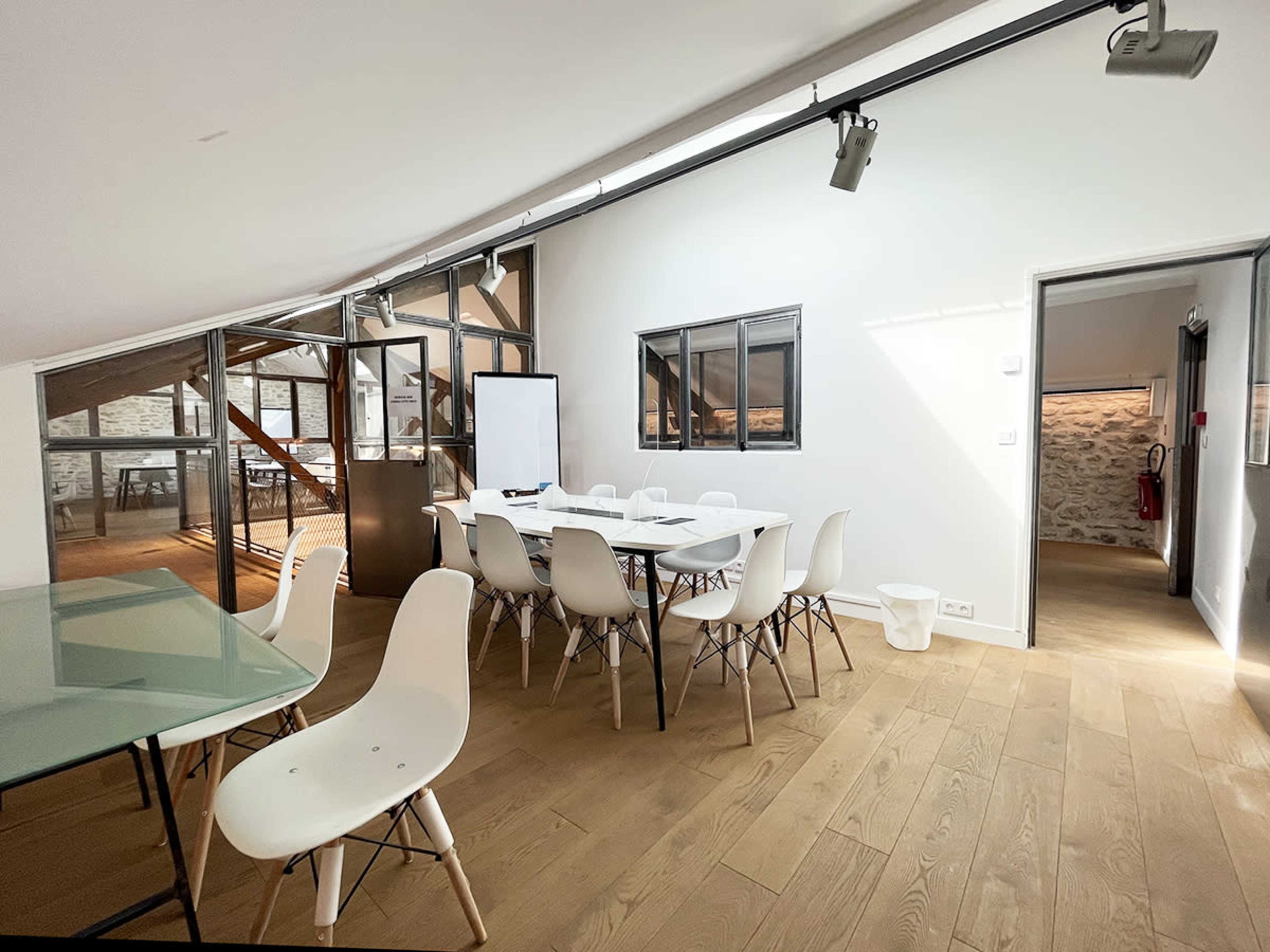 A modern meeting room with a large table, white chairs, and large windows letting in natural light.