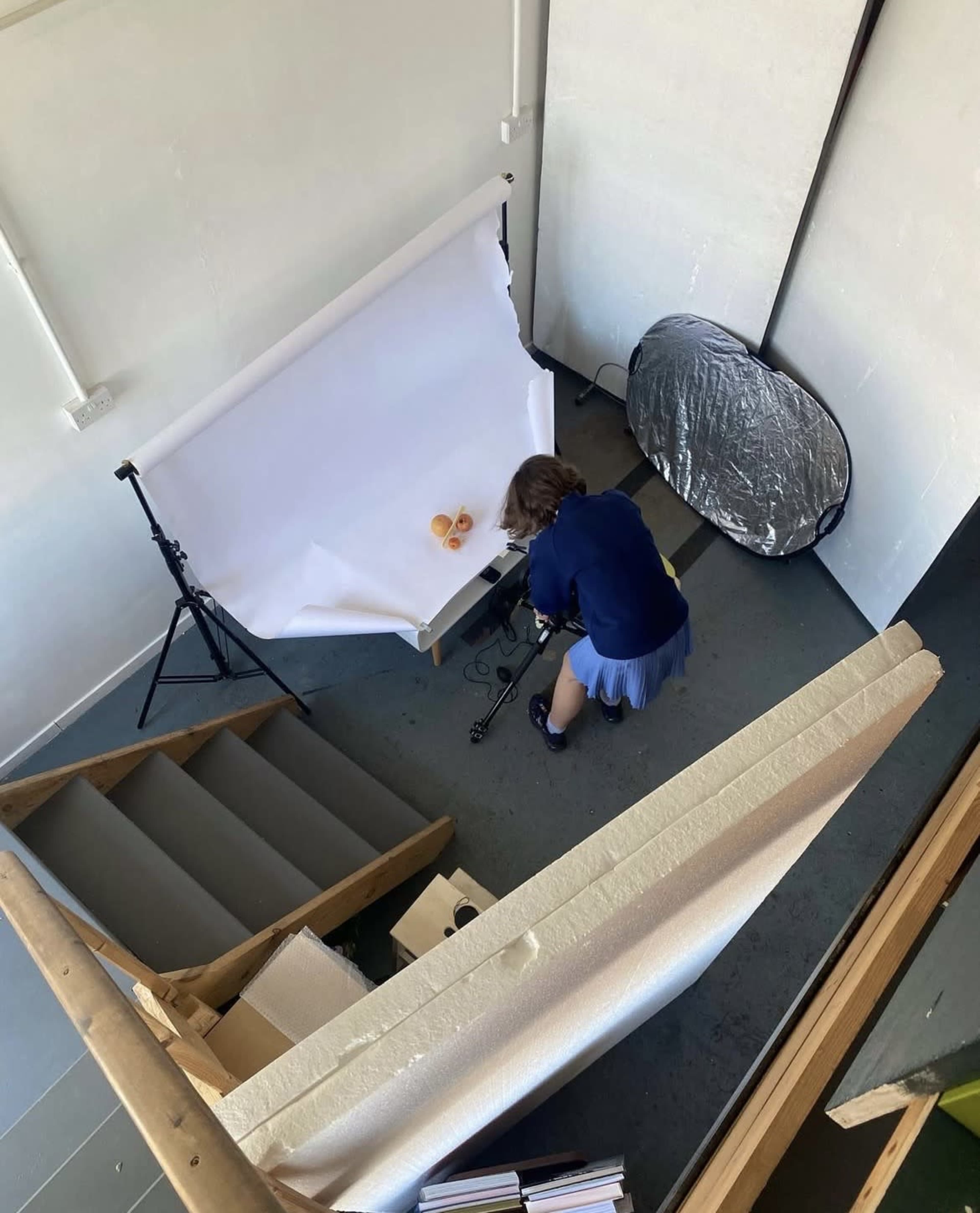 A person is setting up a photography shoot with a backdrop and lighting equipment in a well-lit room.