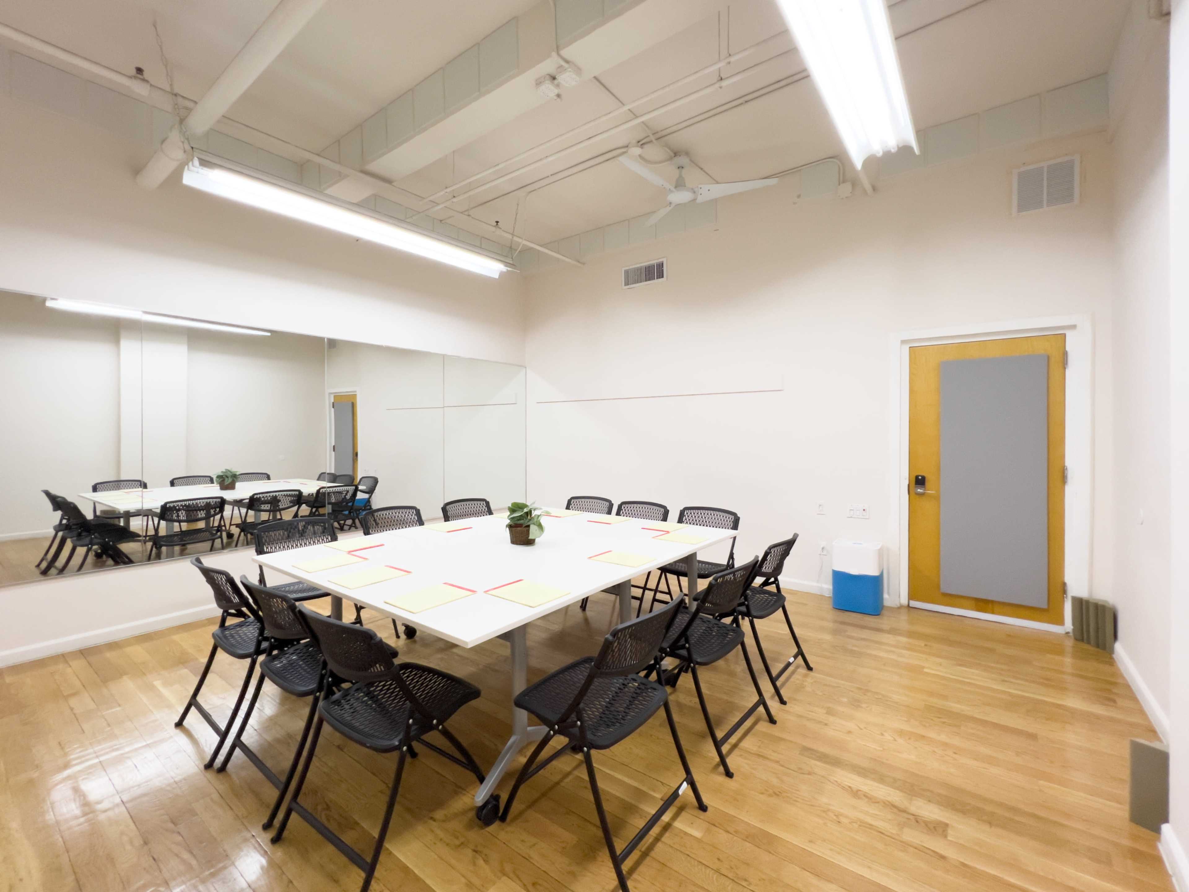 The image shows a meeting room with a large table surrounded by black chairs, a potted plant centerpieces, and a mirror on one wall.