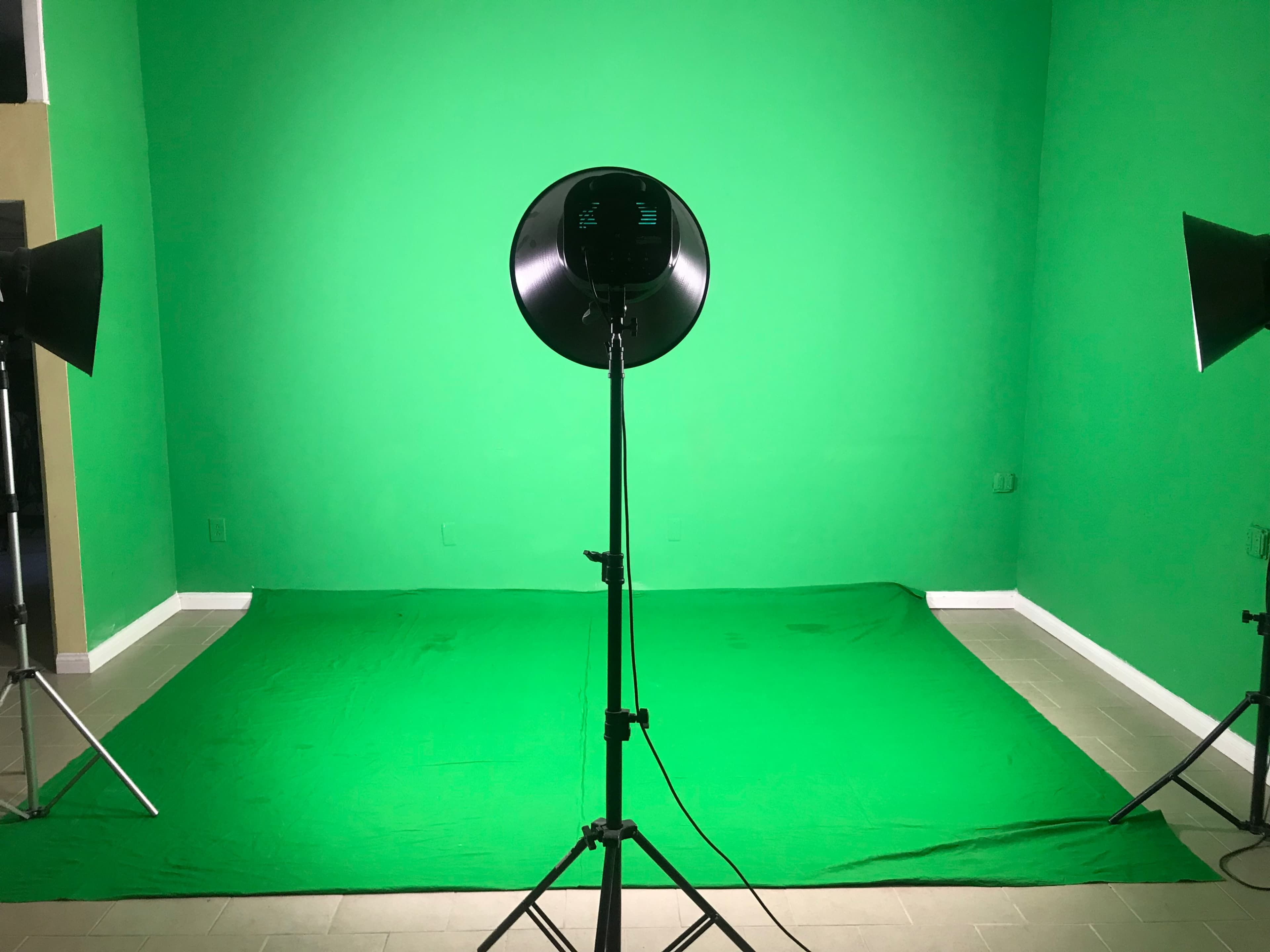 A green screen setup with a green backdrop, a round light source on a stand, and two light fixtures positioned on either side.