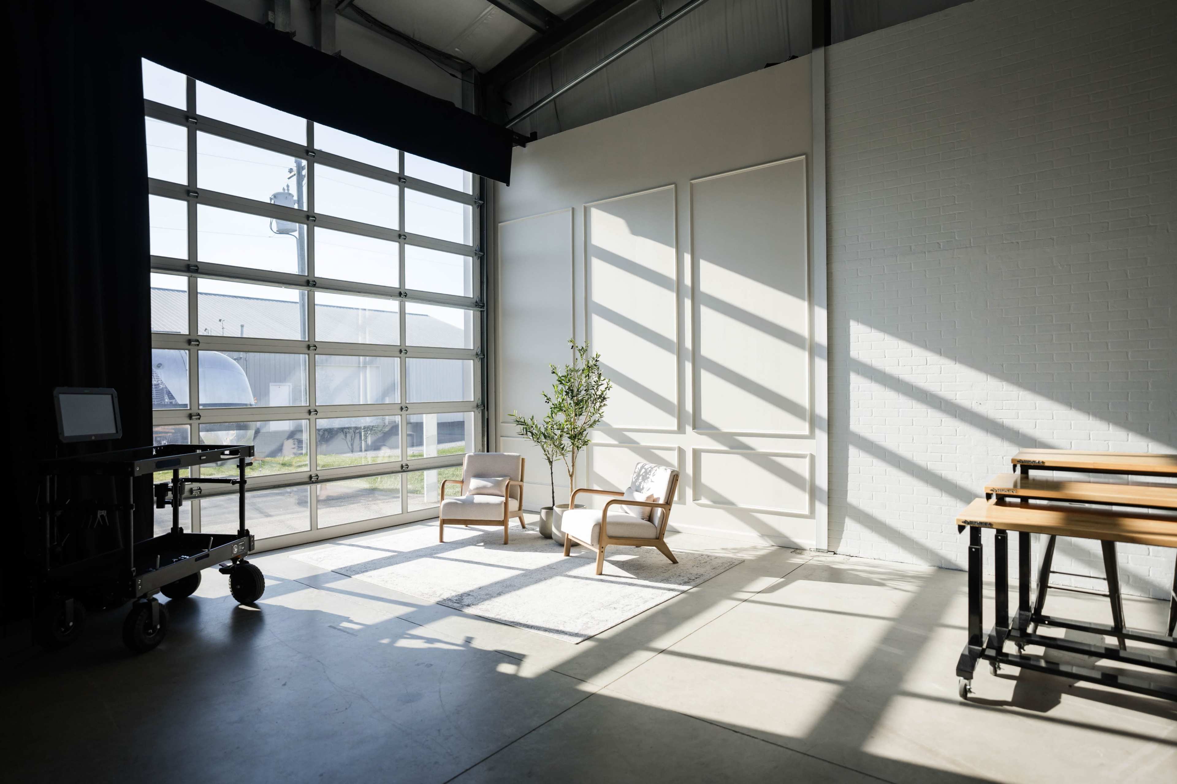 A bright interior space with two chairs and a small plant, illuminated by sunlight streaming through large windows.