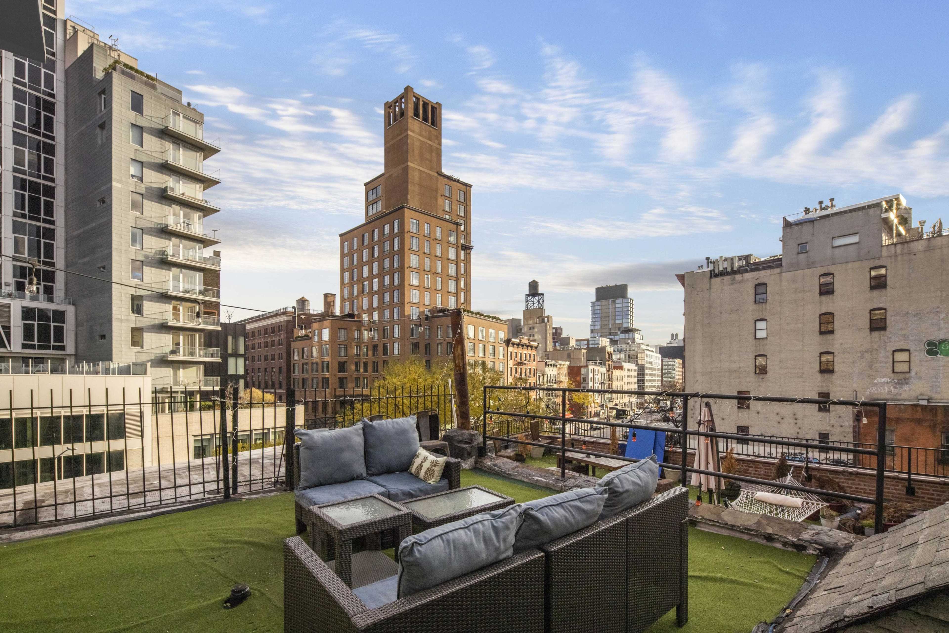 A rooftop terrace features a seating area with a view of city buildings and a cloudy sky in the background.