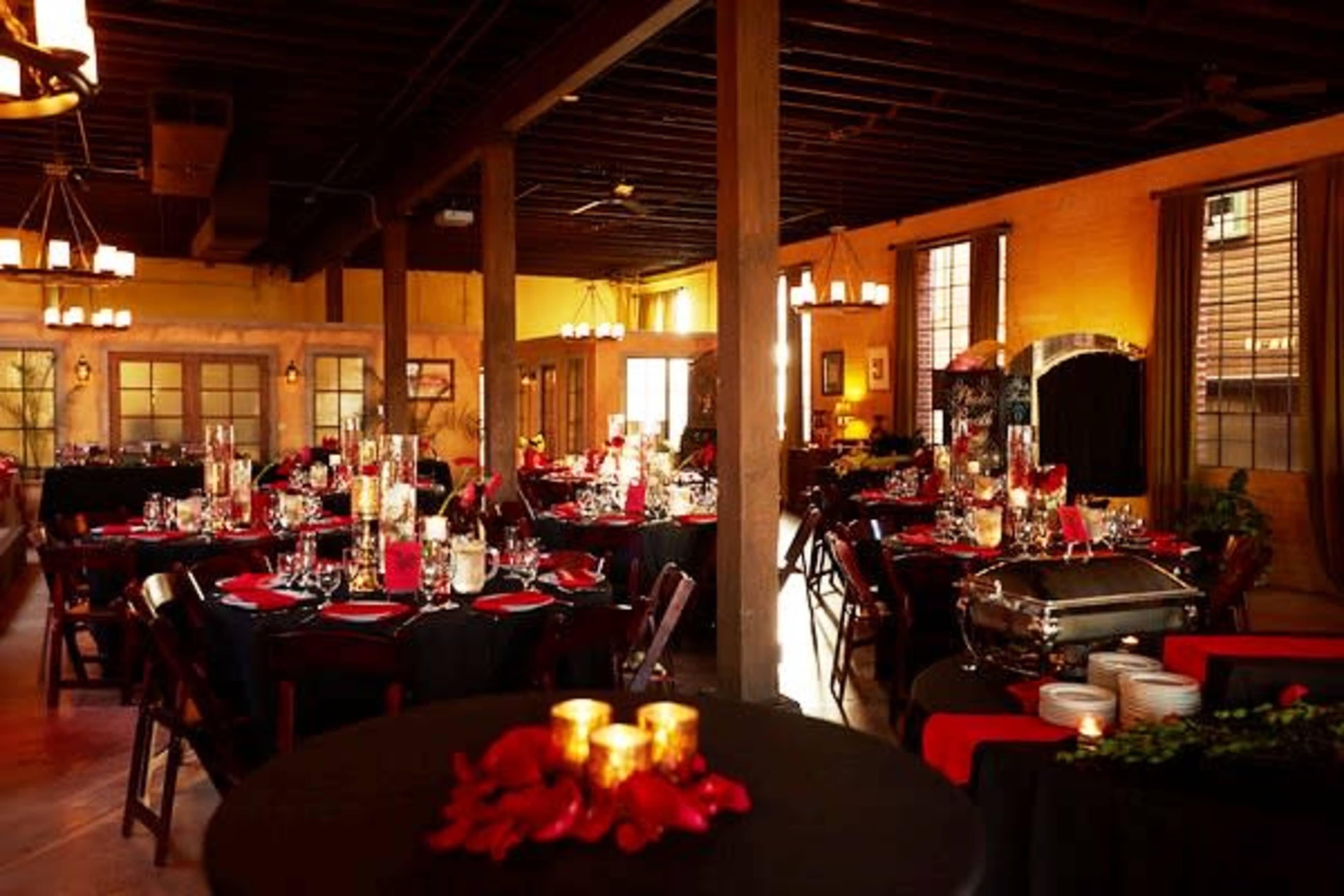 A decorated dining area with black tablecloths, centerpieces featuring candles and flowers, and set tables for an event.