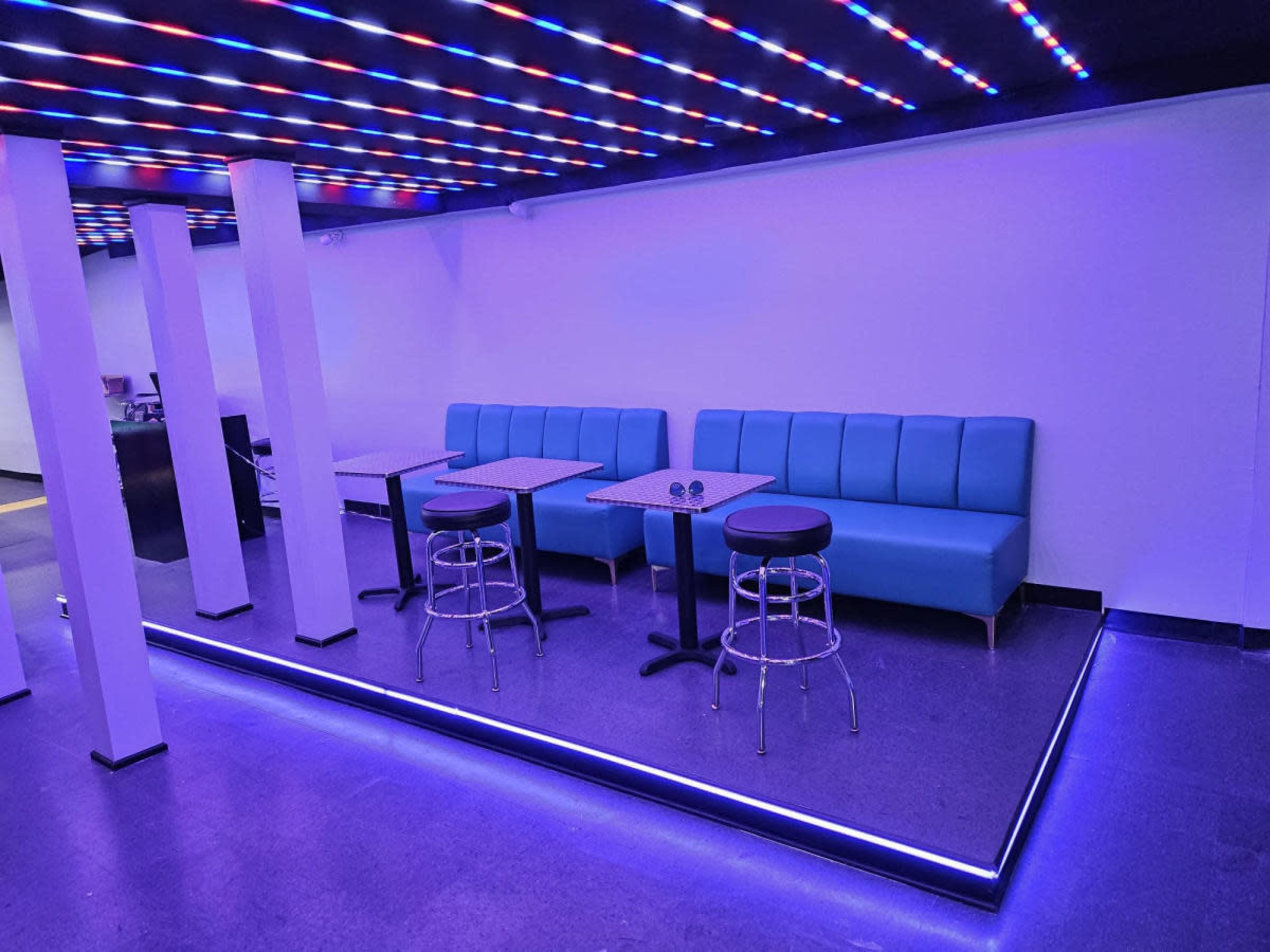 The image shows a modern lounge area with blue seating, tables, and illuminated flooring.