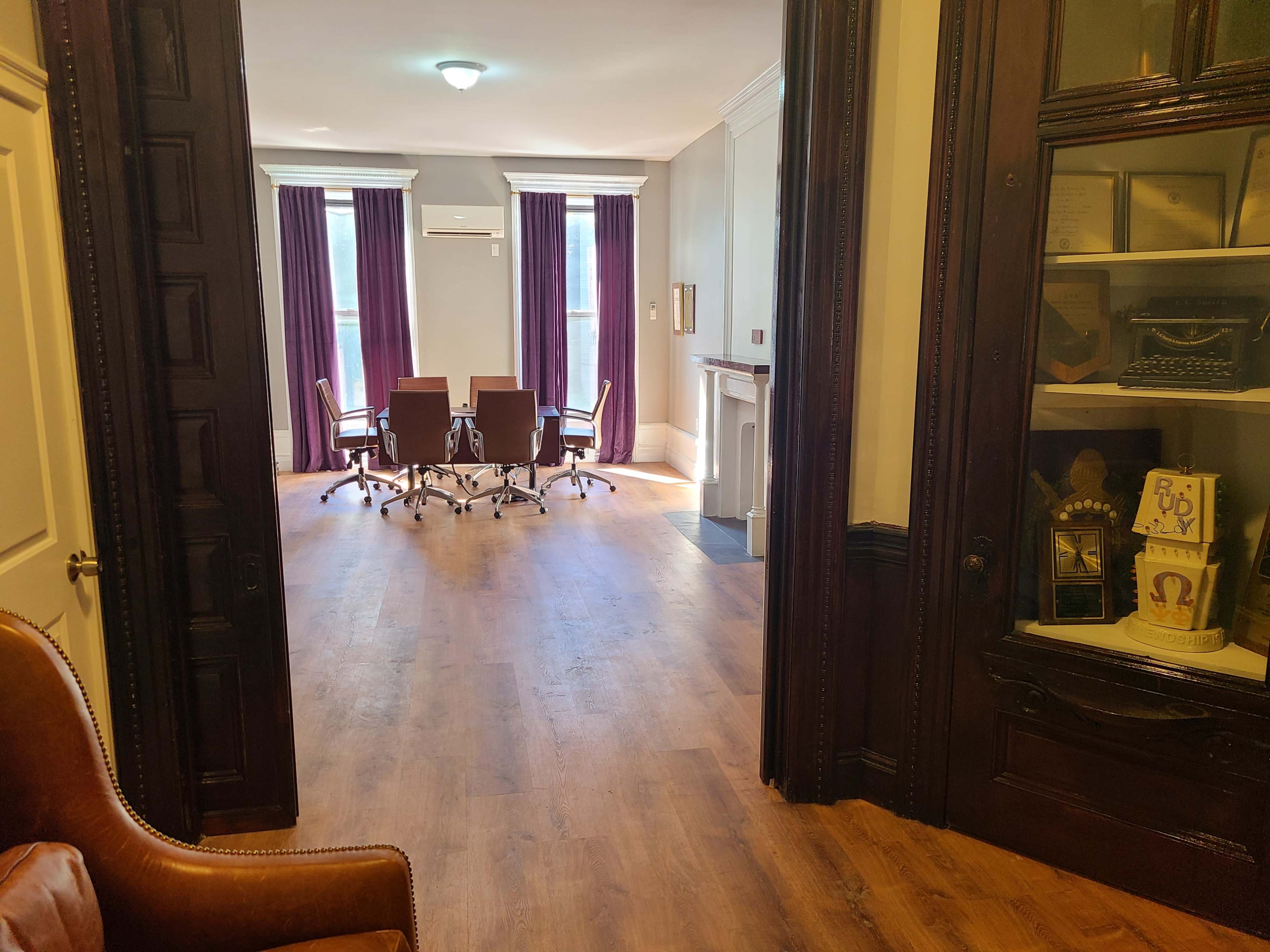 The image shows a well-lit office space with a conference table and chairs, framed by dark wooden doors and a display cabinet on the right.