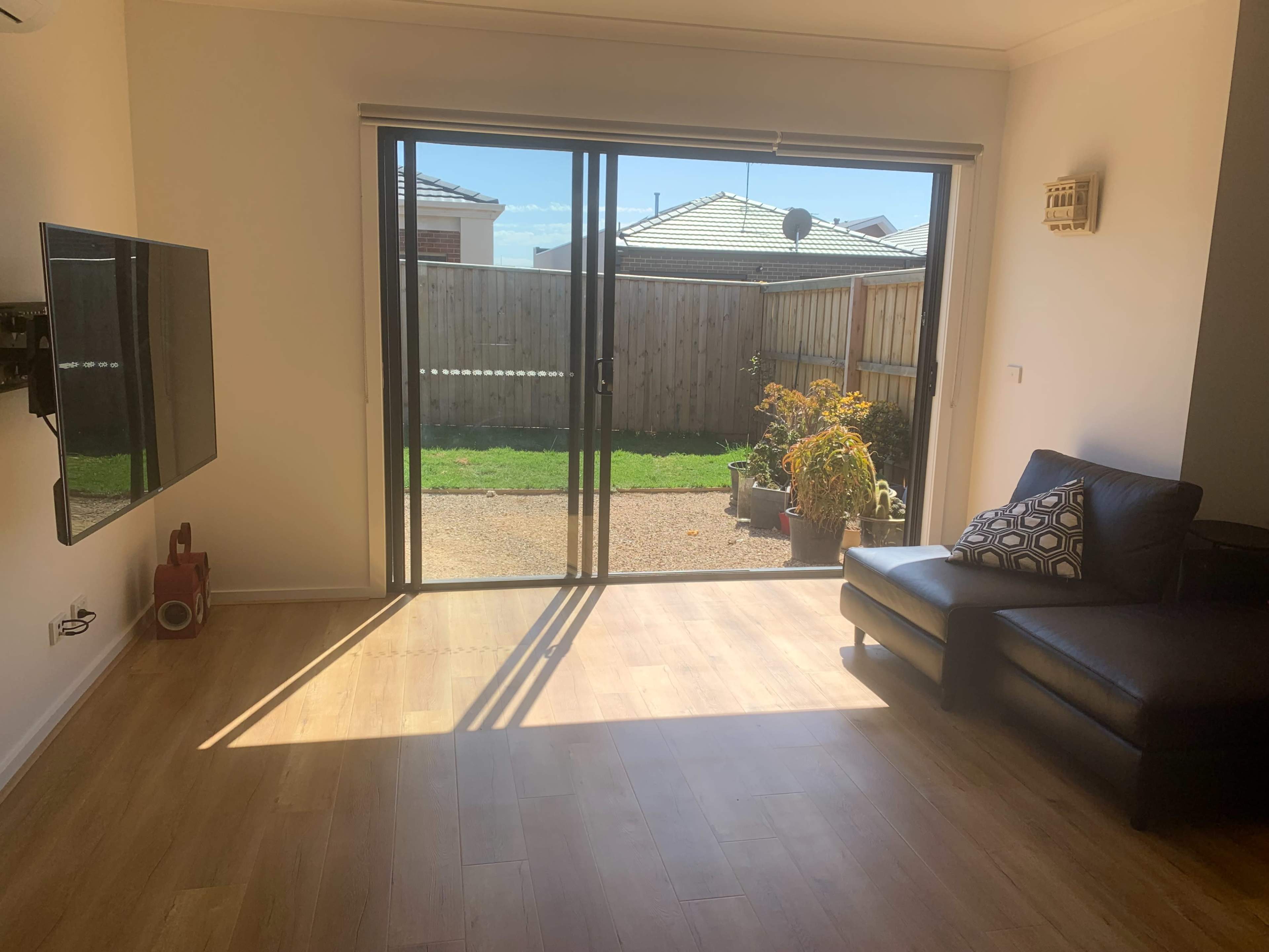 A living room with a black leather couch, a television mounted on the wall, and large sliding glass doors leading to a backyard.