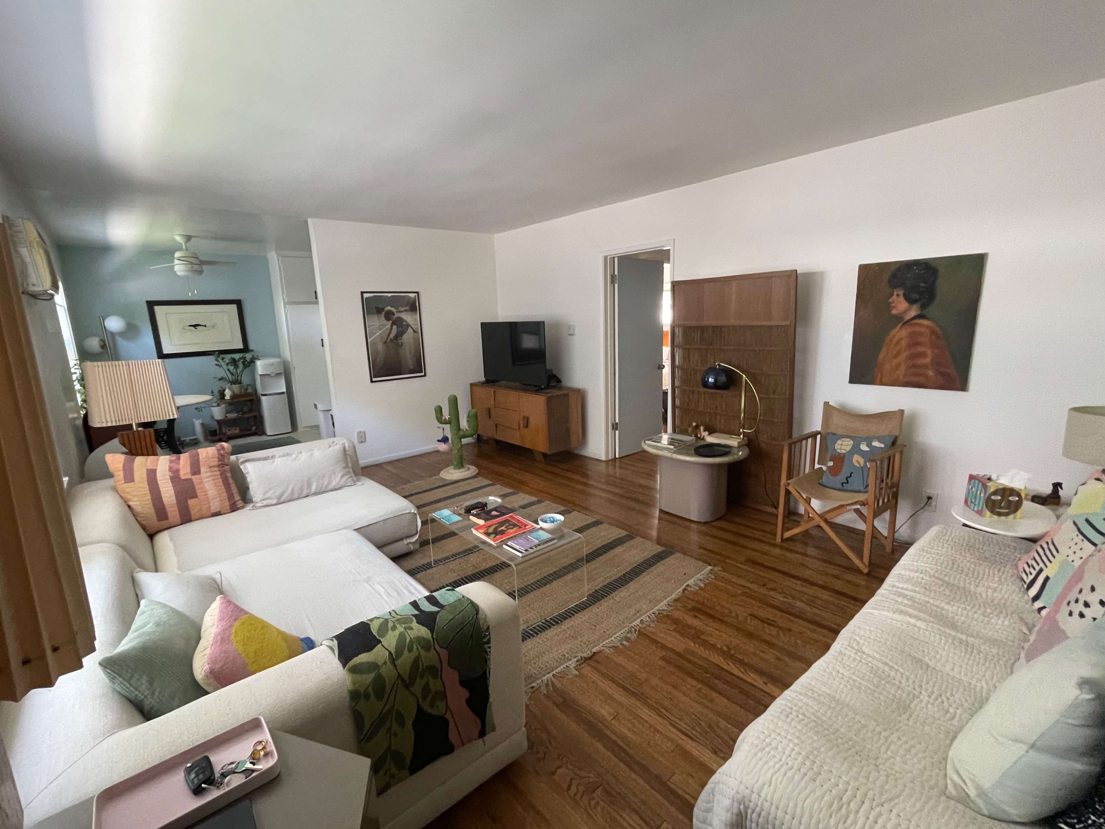 The living room features two sofas, a coffee table with magazines, a rug, and various decorative items, including a lamp and a cactus.