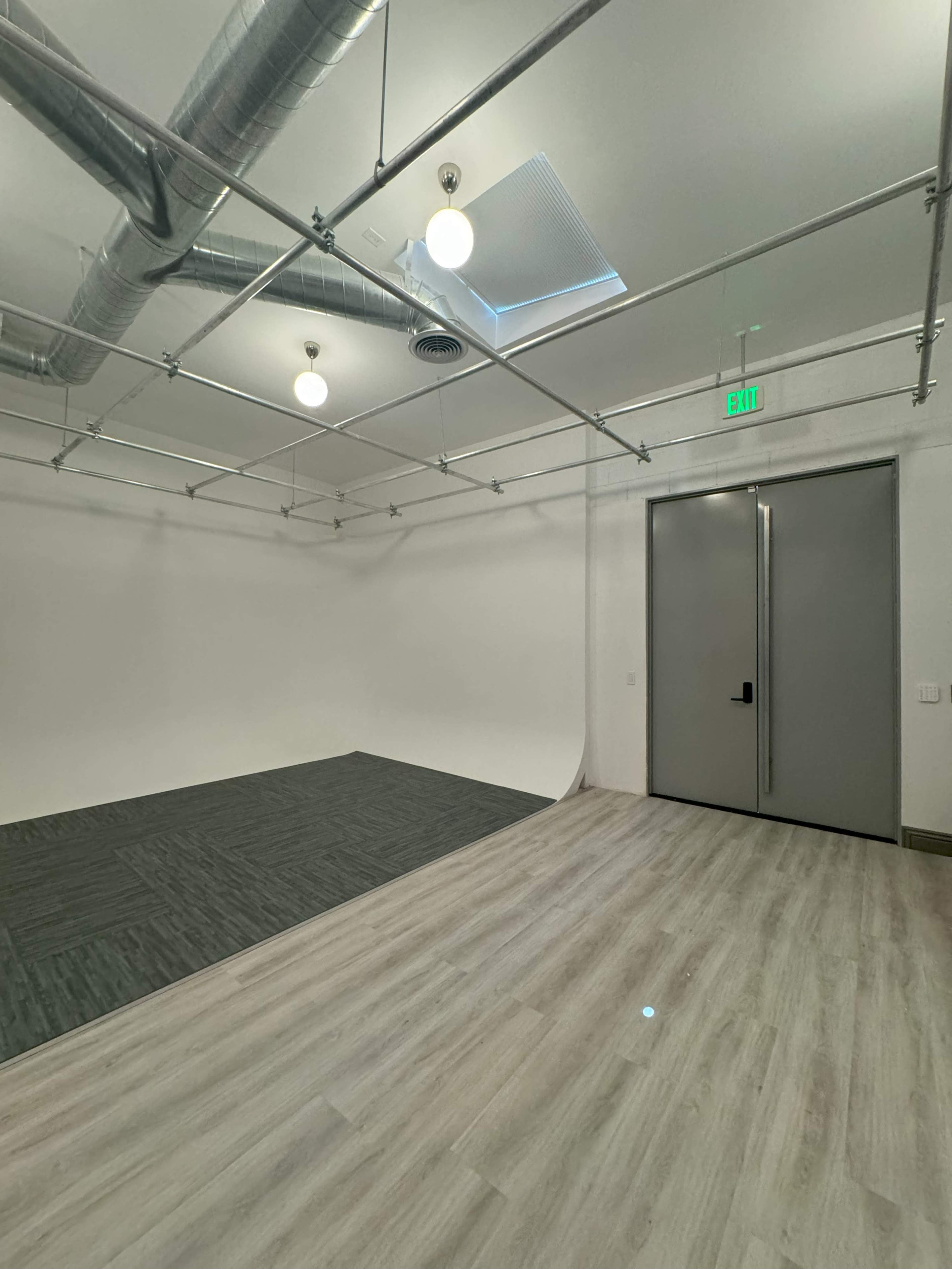 An empty studio space with a smooth, light-colored floor, a white backdrop area, and exposed ductwork on the ceiling.