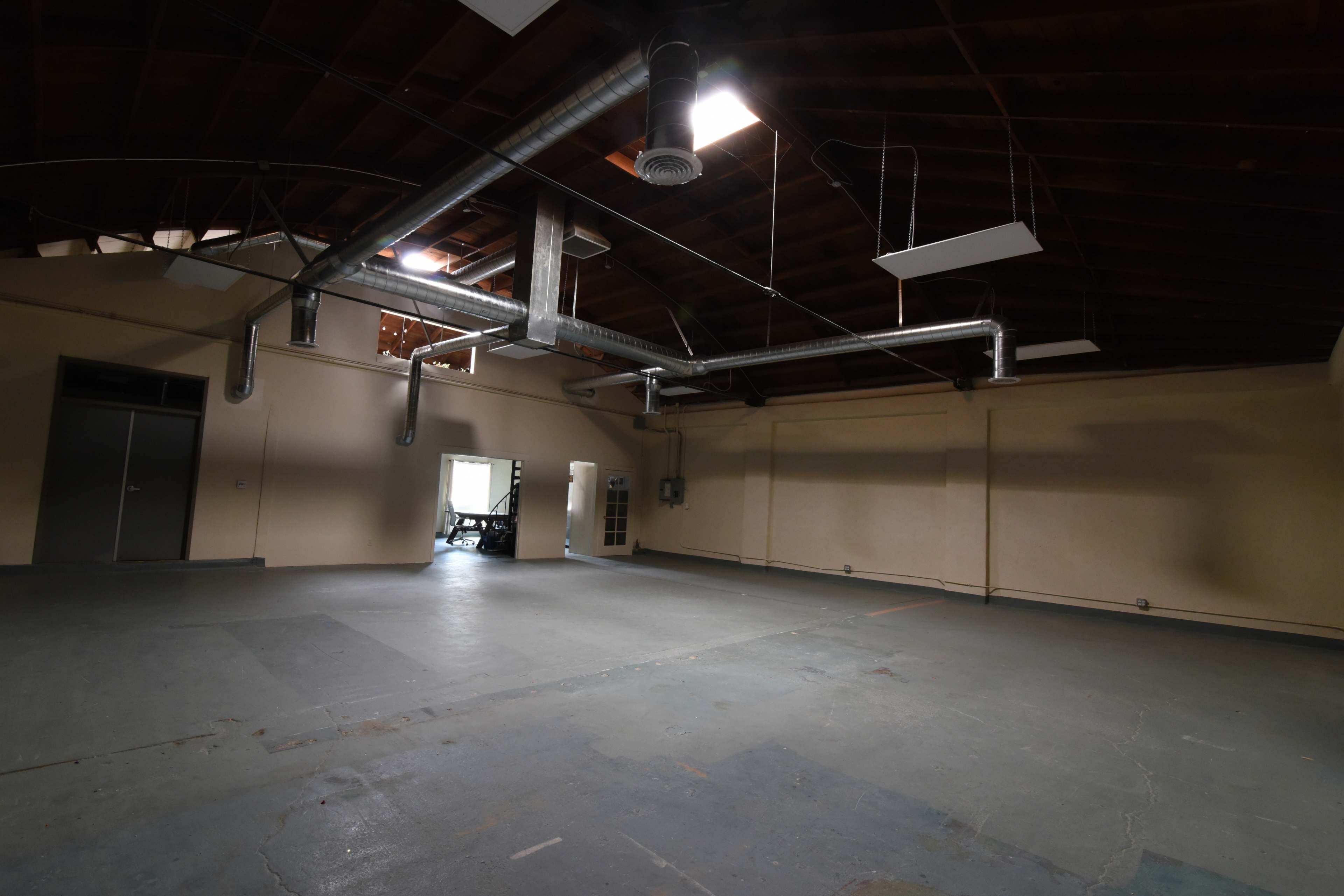 A spacious, empty room with a high ceiling, exposed ductwork, and concrete flooring.