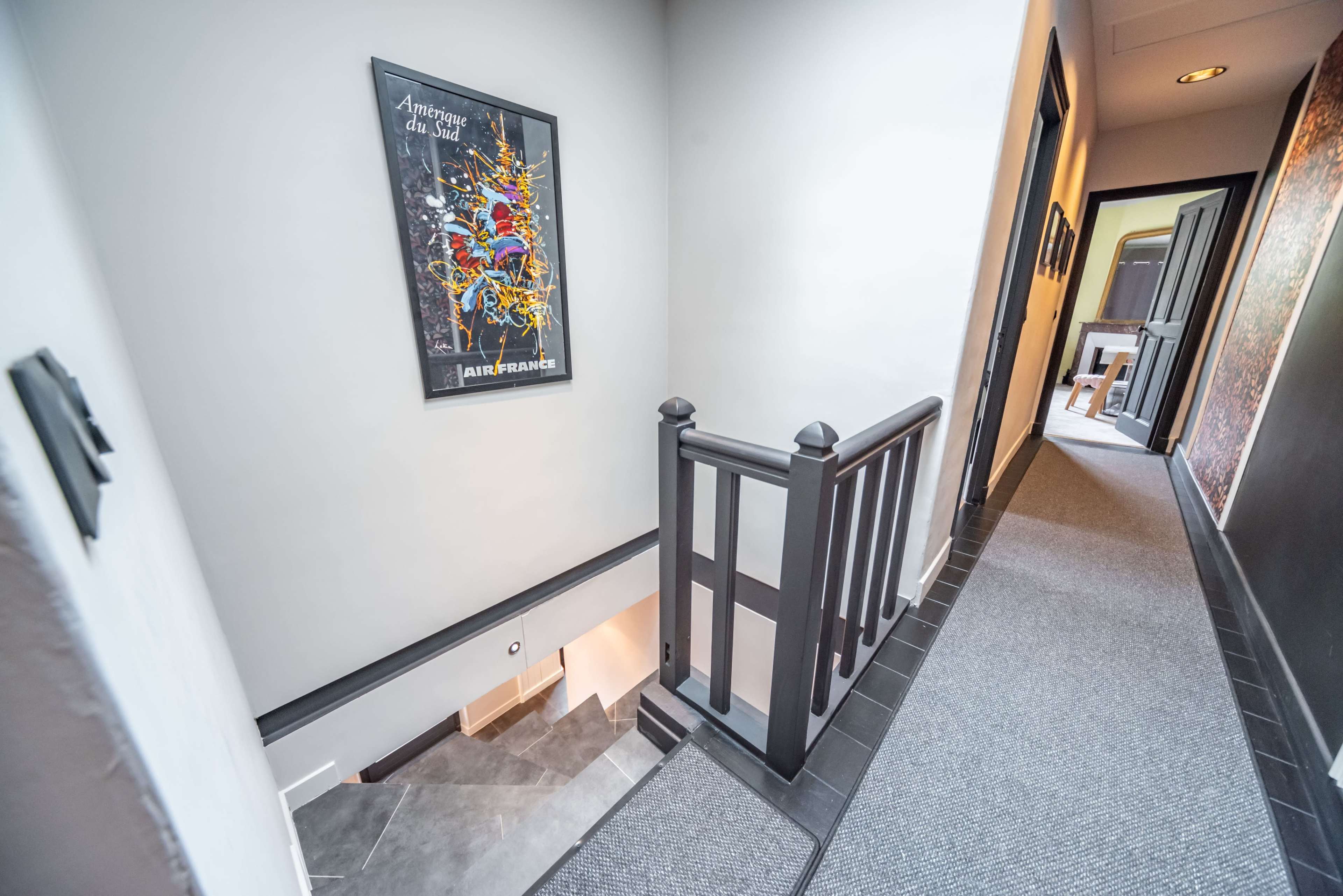 A staircase leads down to a hallway with a framed art poster on the wall and carpeted flooring.