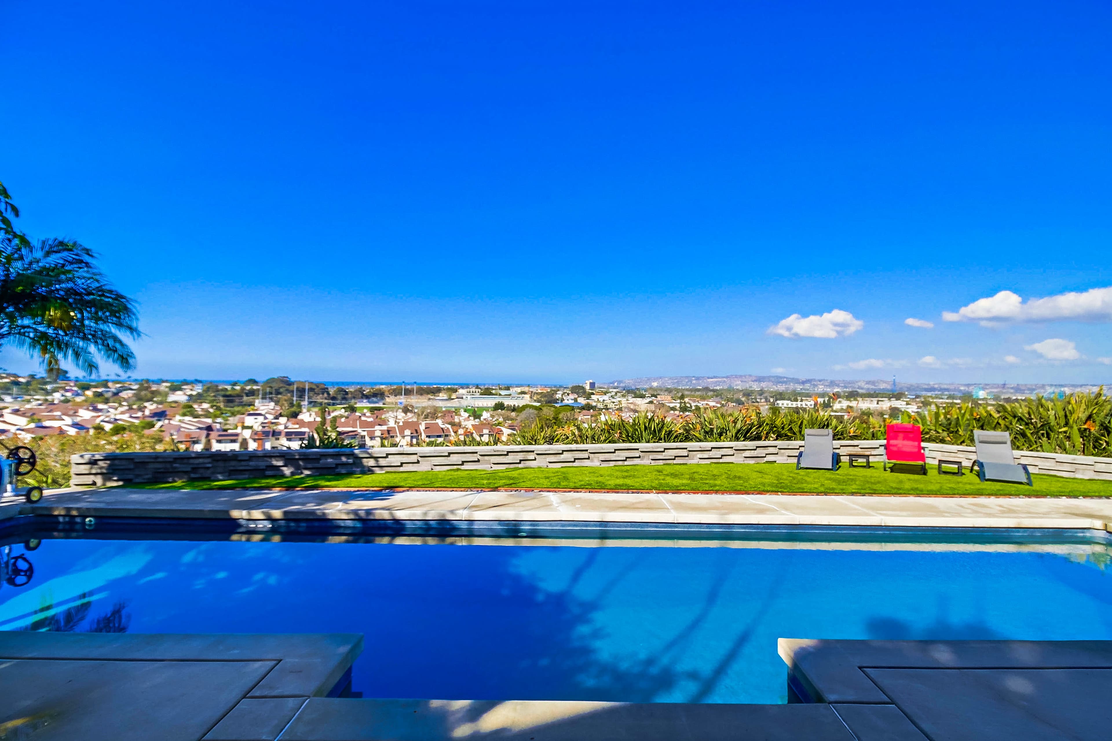 A swimming pool with a view overlooking a suburban area and the ocean in the distance.