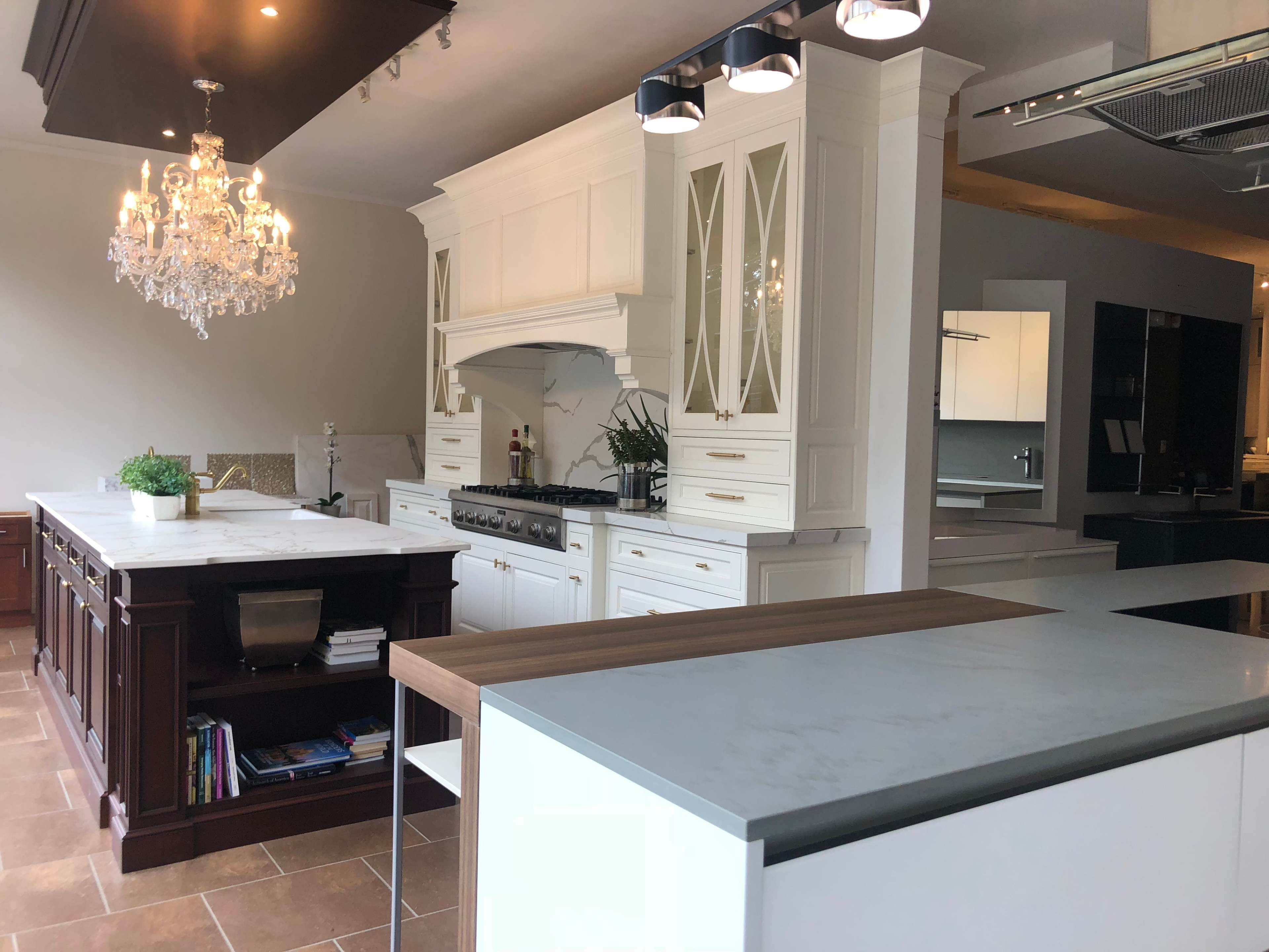 A modern kitchen featuring white cabinetry, a large central island with a wooden and marble counter, and a chandelier overhead.