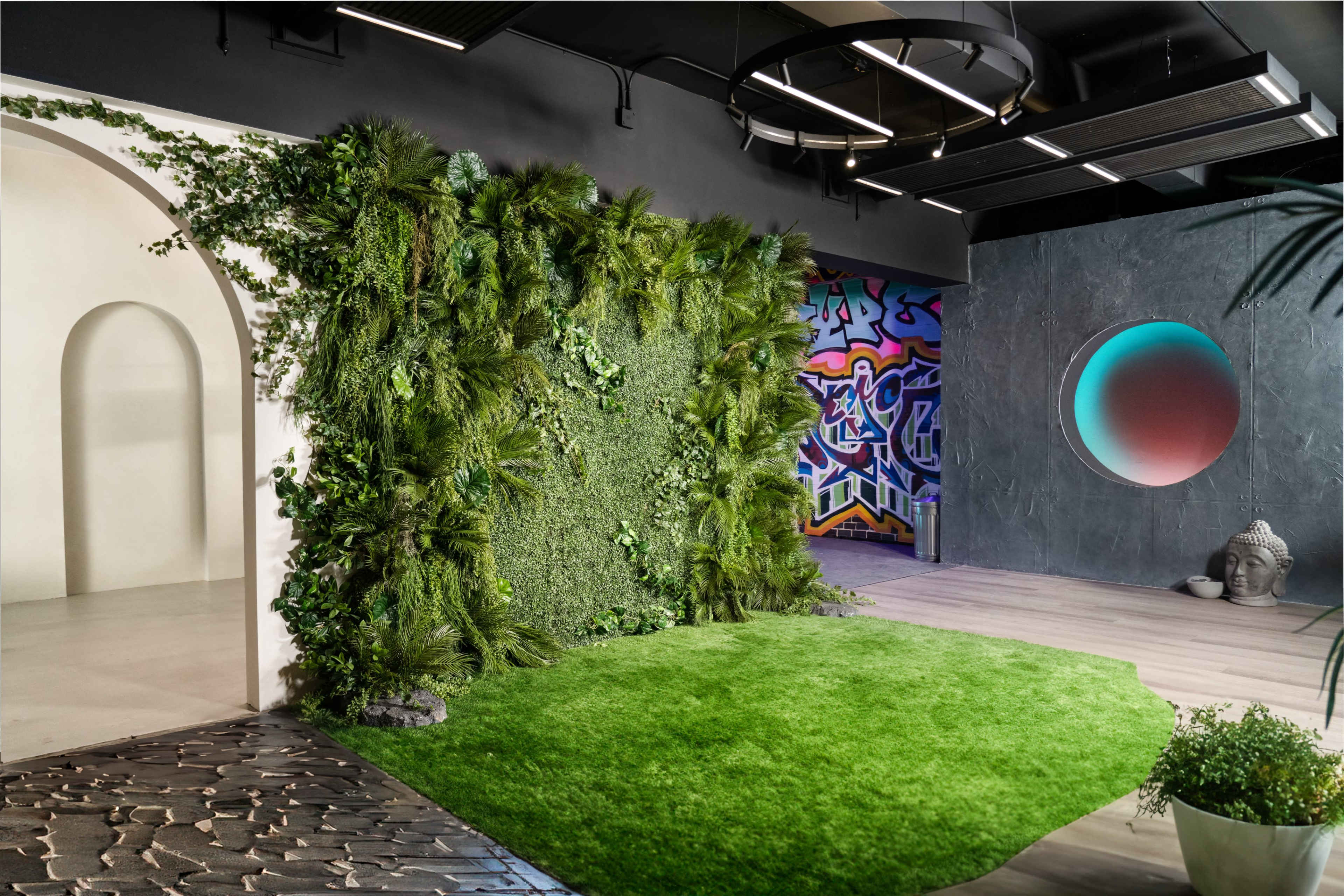 The interior features a living wall of greenery beside a mural with vibrant graffiti, set against a modern design of open spaces and varied textures.