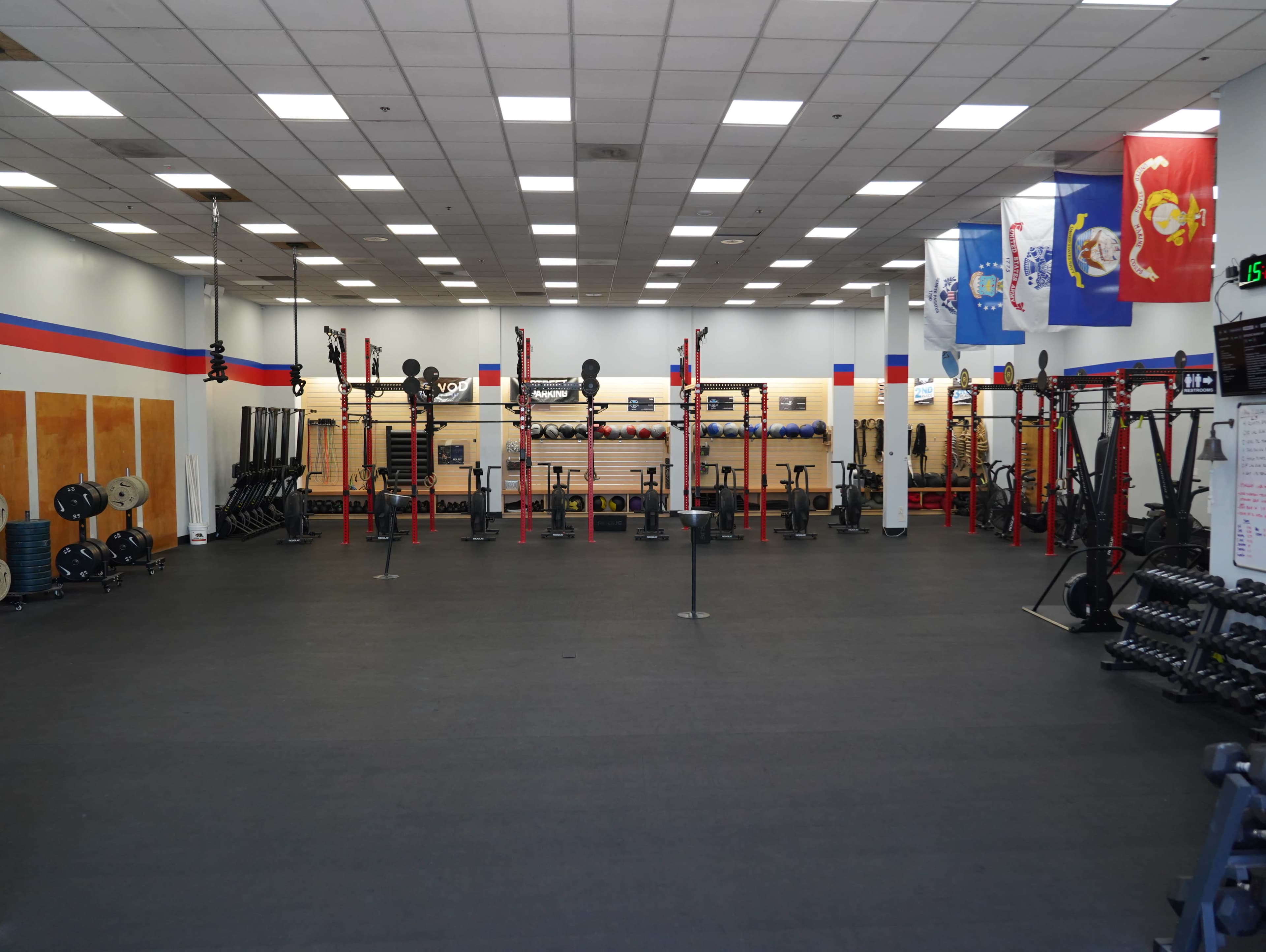 The image shows a spacious gym with multiple weightlifting stations, exercise equipment, and various flags displayed on the walls.