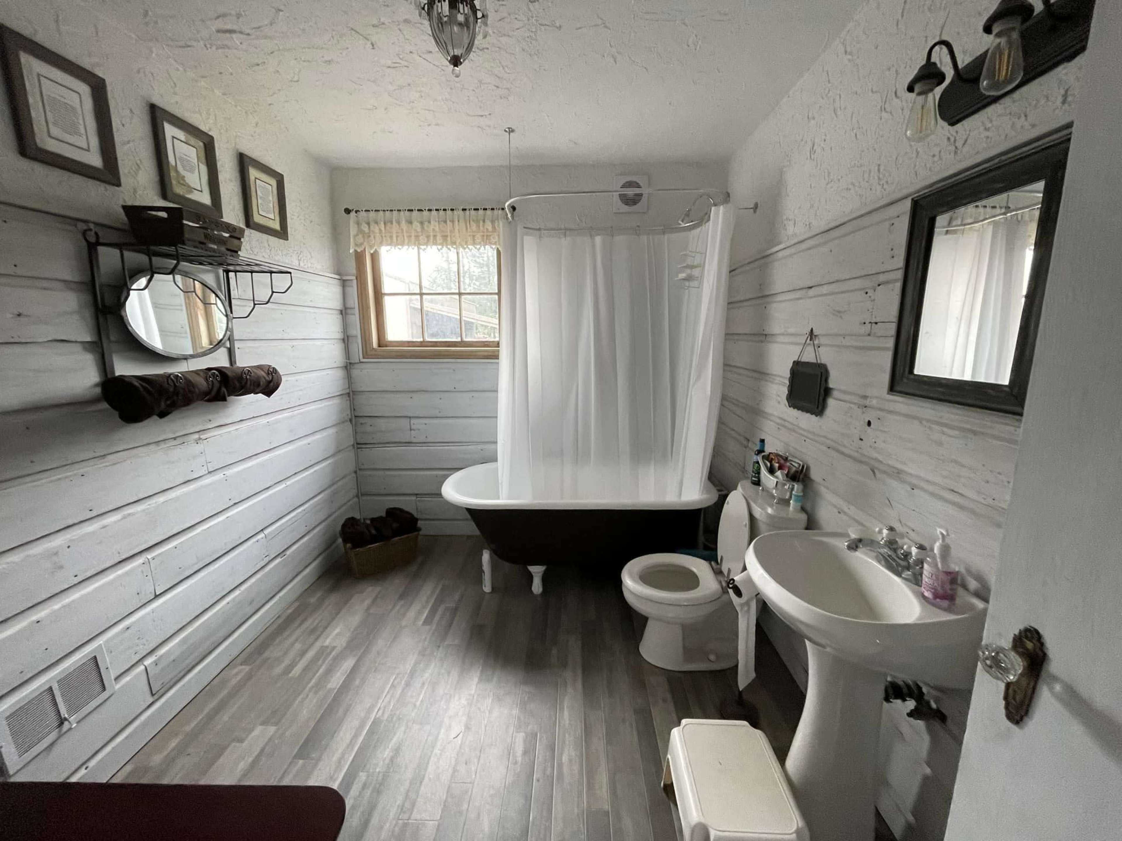 A bathroom featuring a clawfoot bathtub, a toilet, a sink, and wooden paneling on the walls.