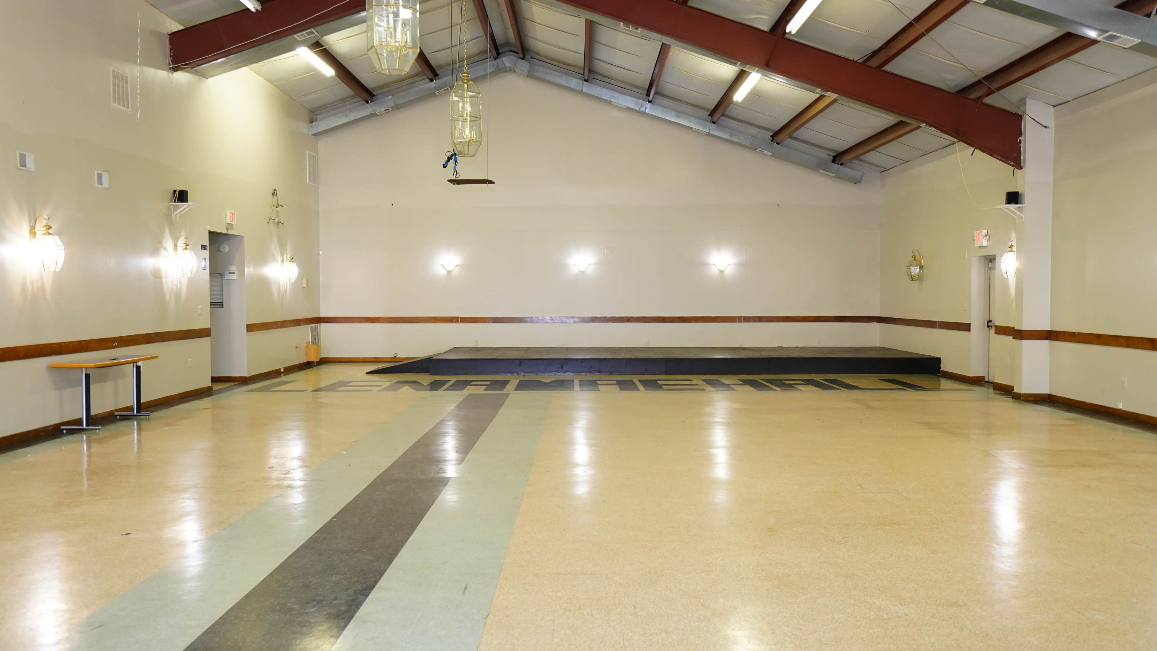 A spacious, empty hall with a raised stage at one end and a patterned floor.