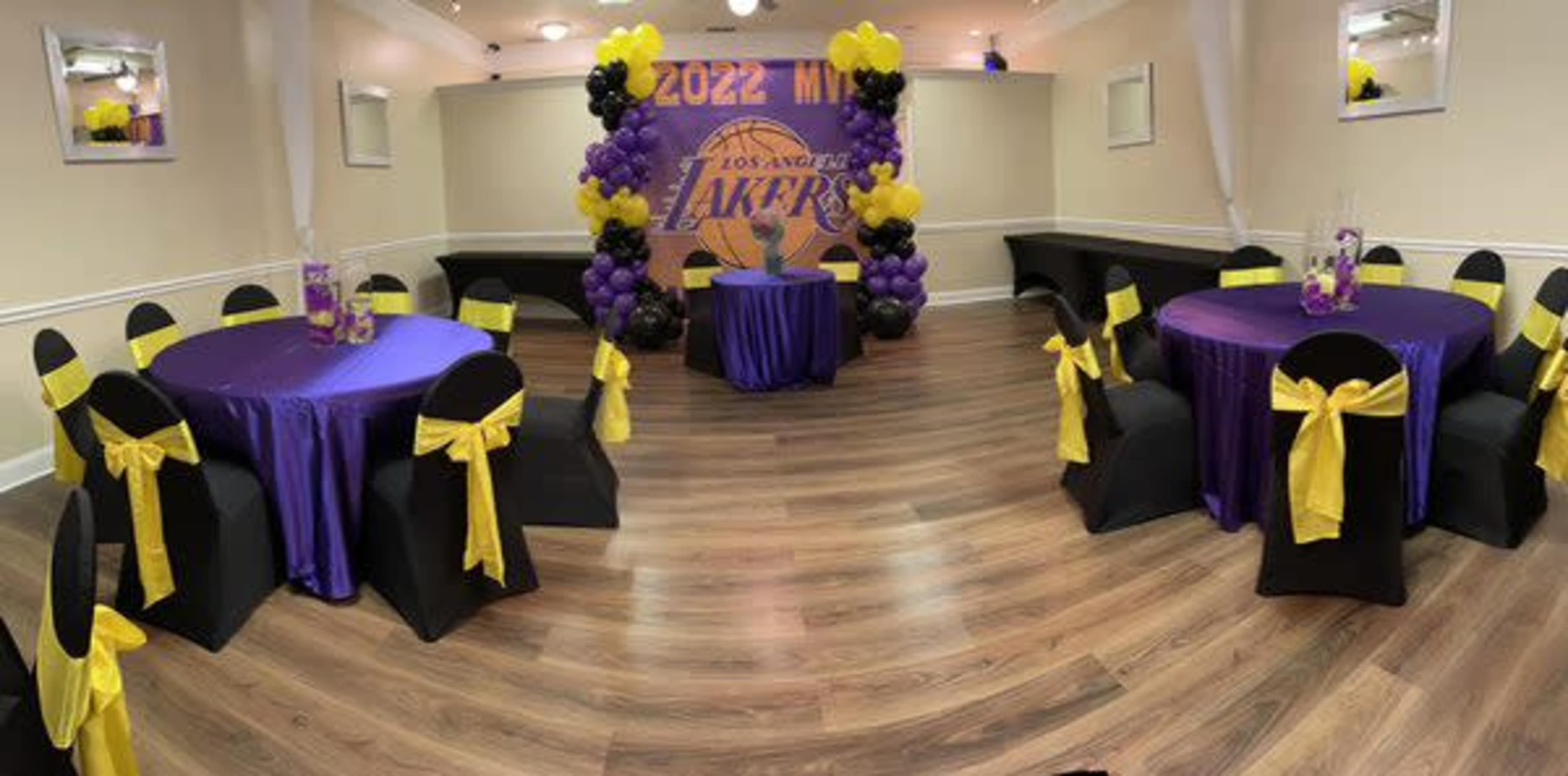 A room decorated for a Los Angeles Lakers event, featuring purple and gold table settings and balloon arrangements.