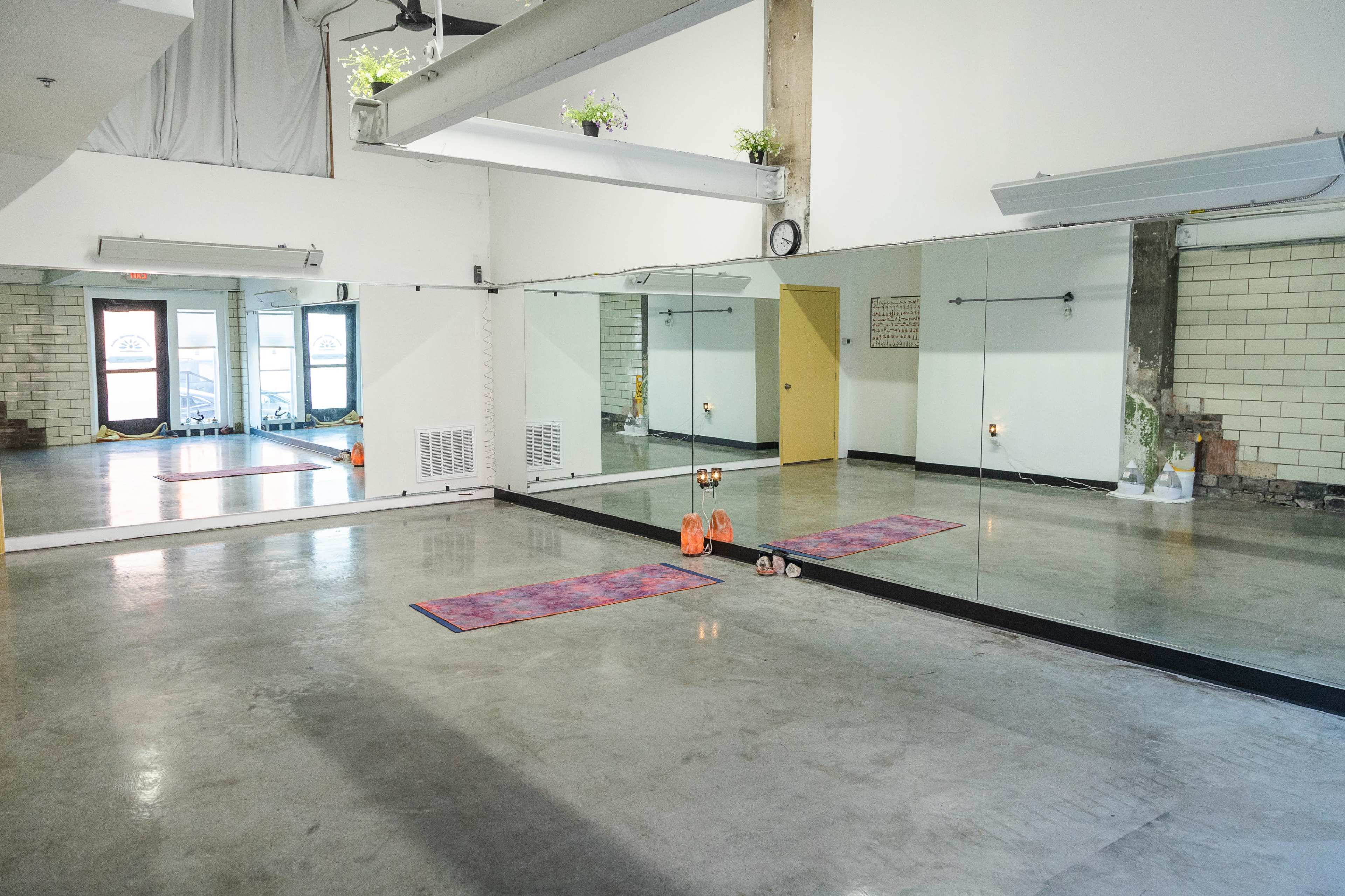 A spacious room with mirrored walls, two exercise mats, and dumbbells on the floor.