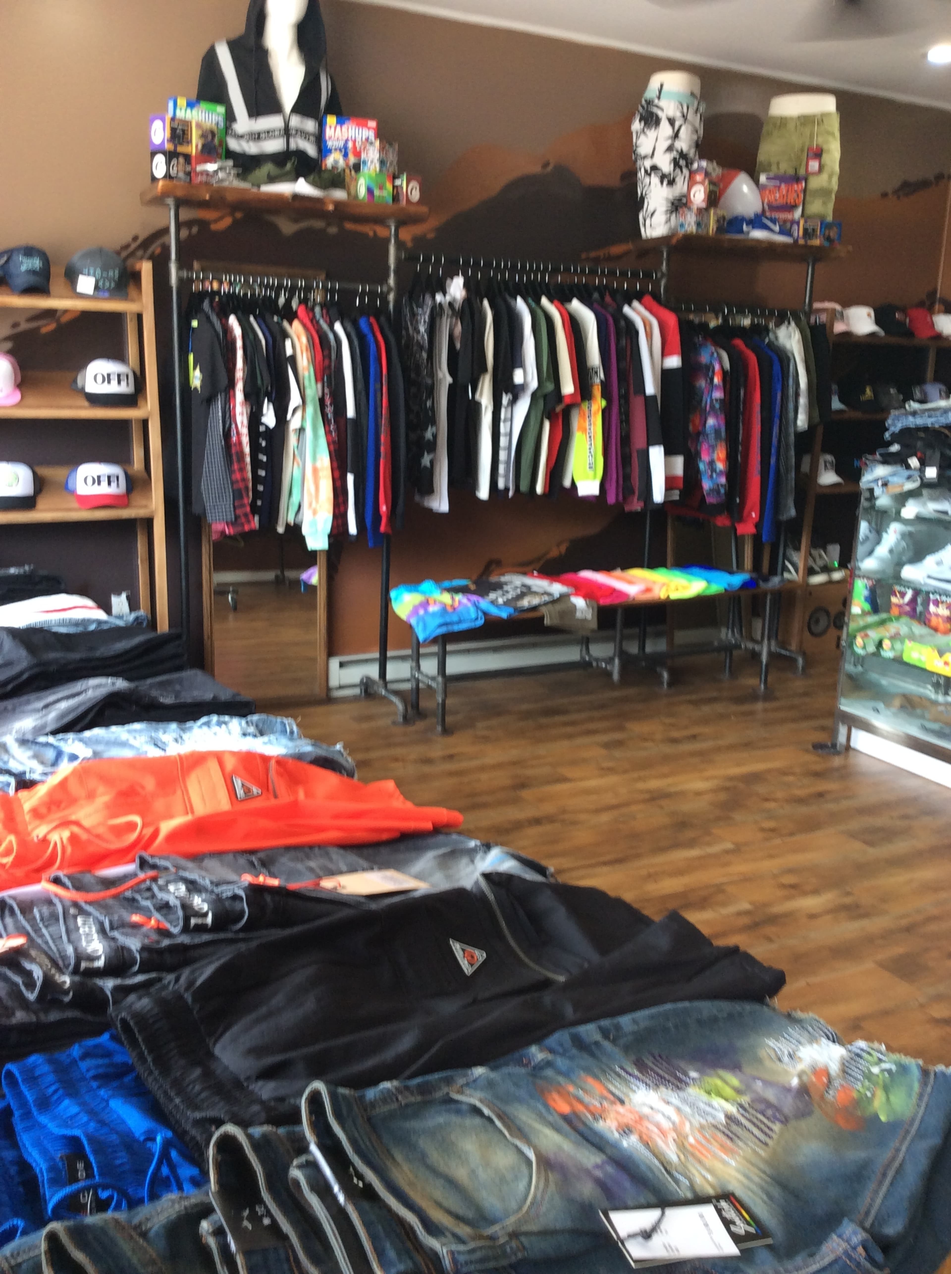 The image shows a clothing store with a variety of colorful apparel displayed on racks and tables, including shirts, pants, and accessories.