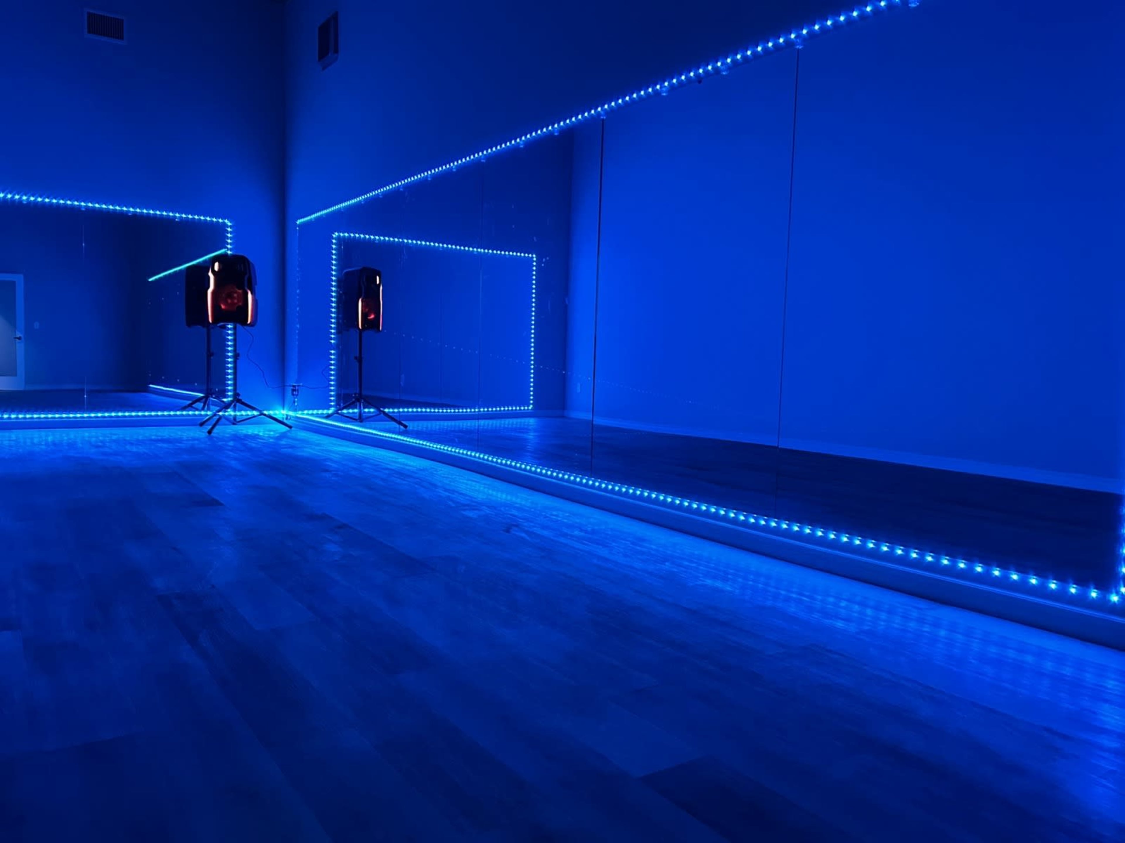 A dance studio features blue LED lights illuminating mirrored walls and a smooth wooden floor.