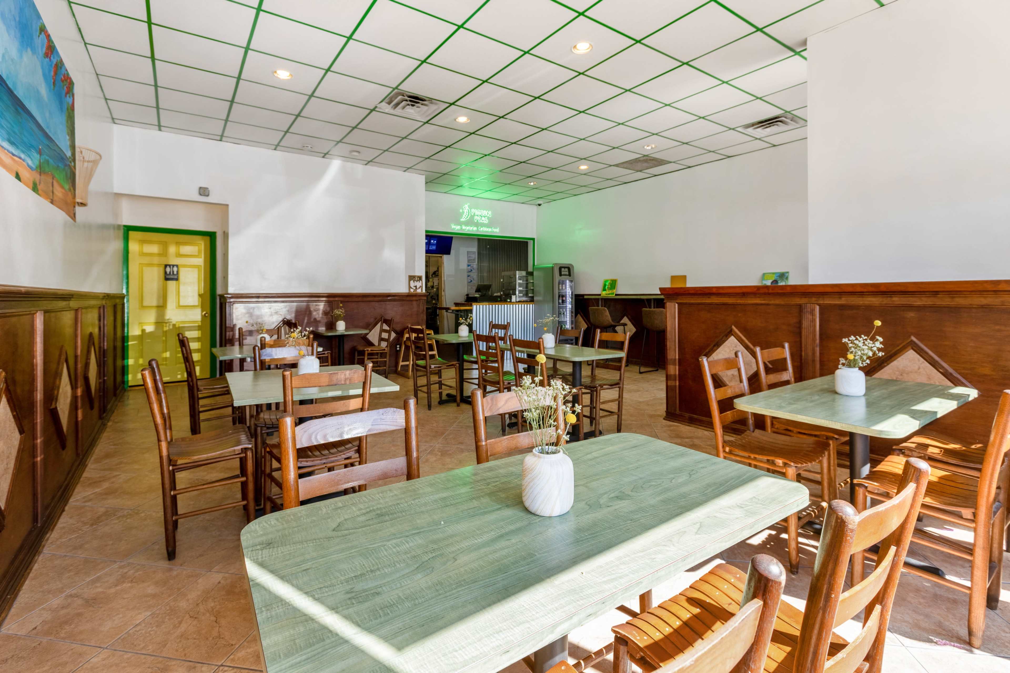 A bright, empty restaurant featuring wooden tables and chairs arranged neatly on tiled flooring.