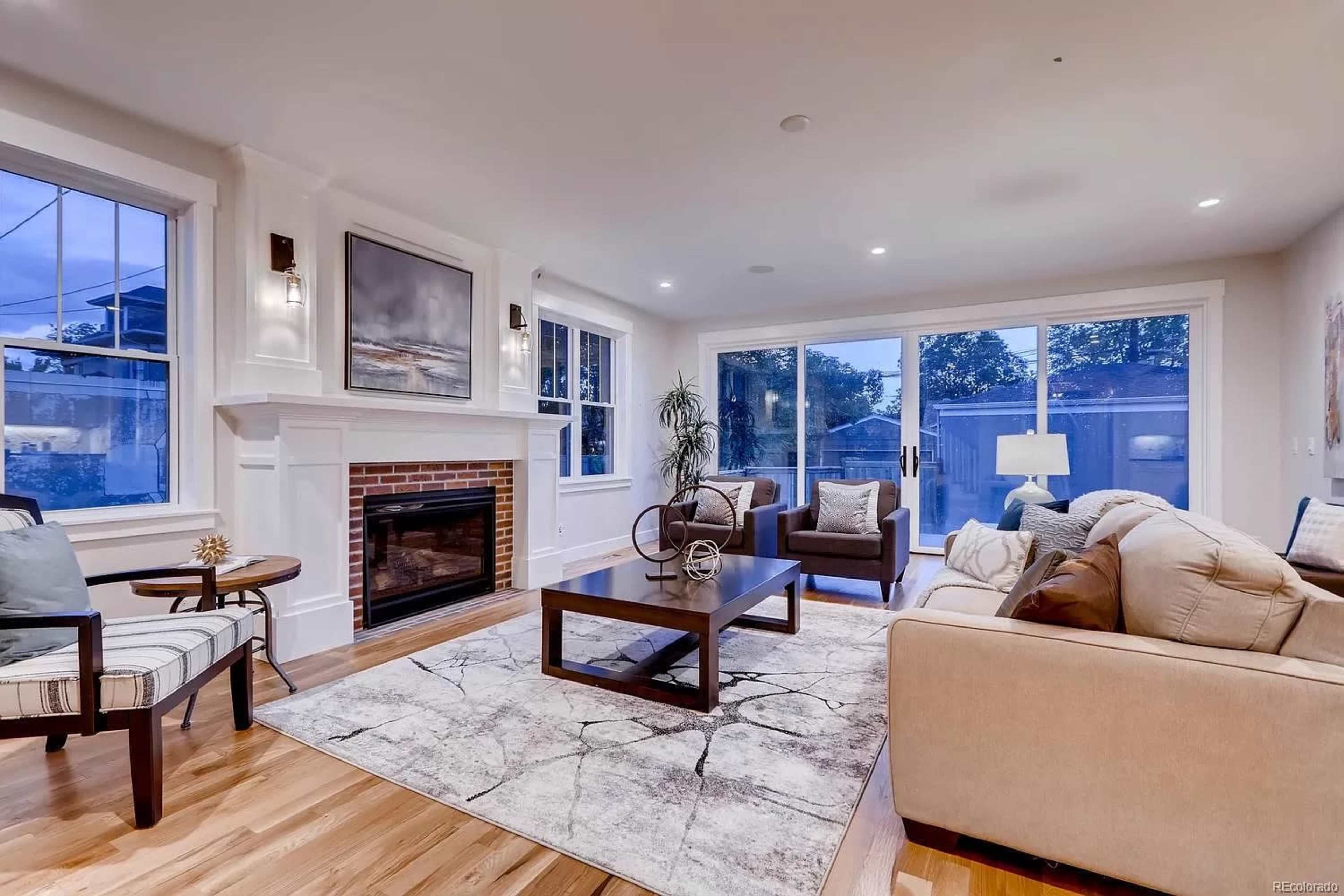 The image shows a modern living room with a fireplace, large windows, and a coffee table placed on a patterned area rug.