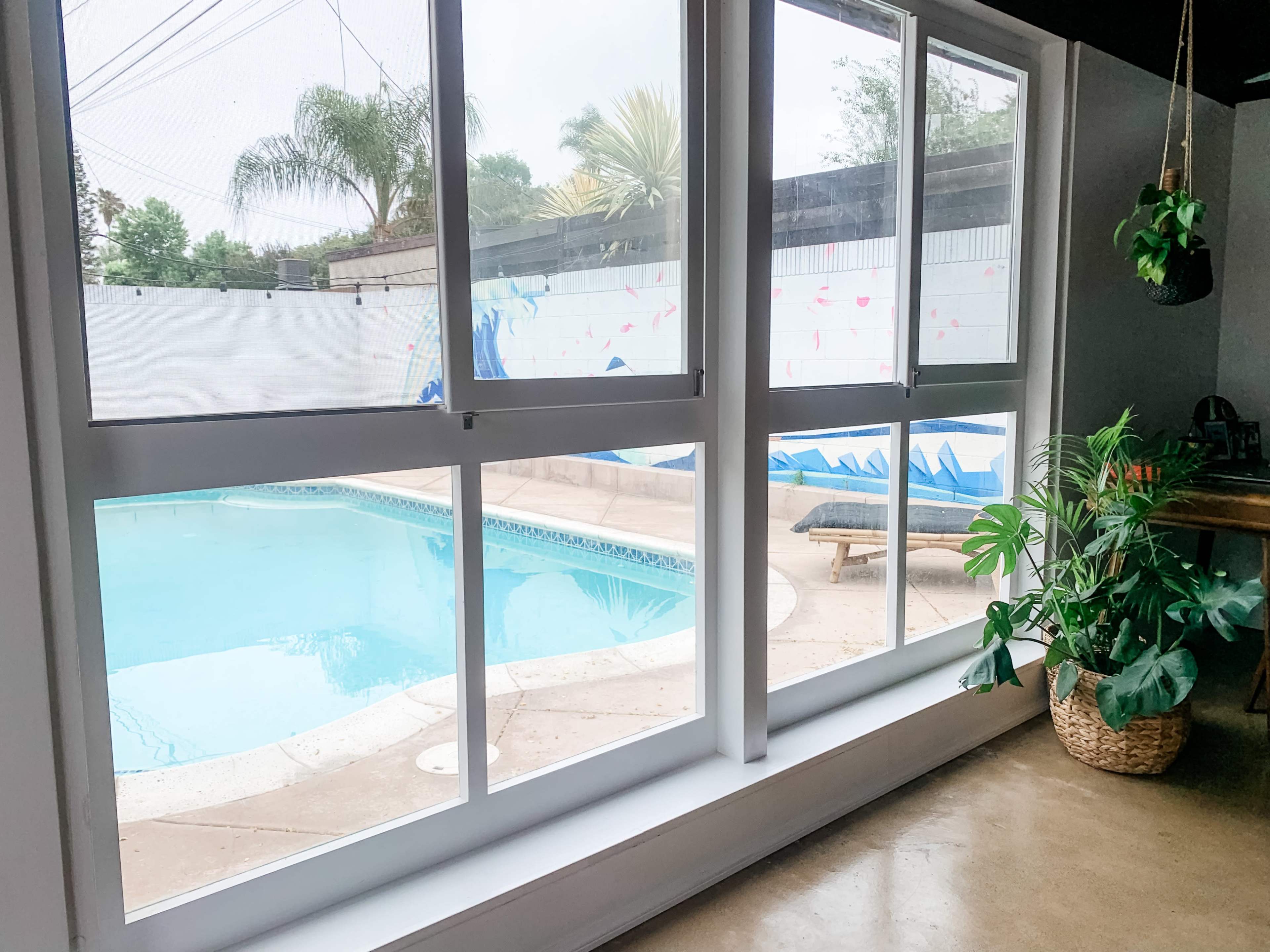 A view of a swimming pool surrounded by a patio, visible through large glass windows.