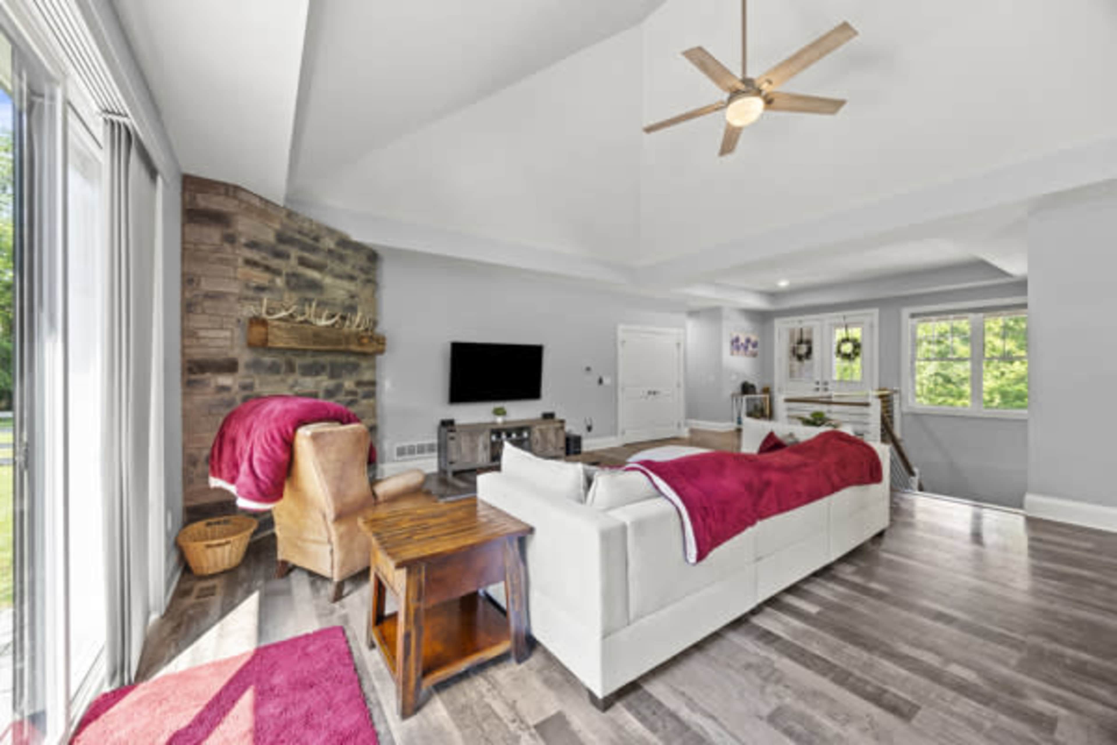 The image shows a modern living room with a white sectional sofa, a wooden side table, a stone accent wall, and large windows allowing natural light.
