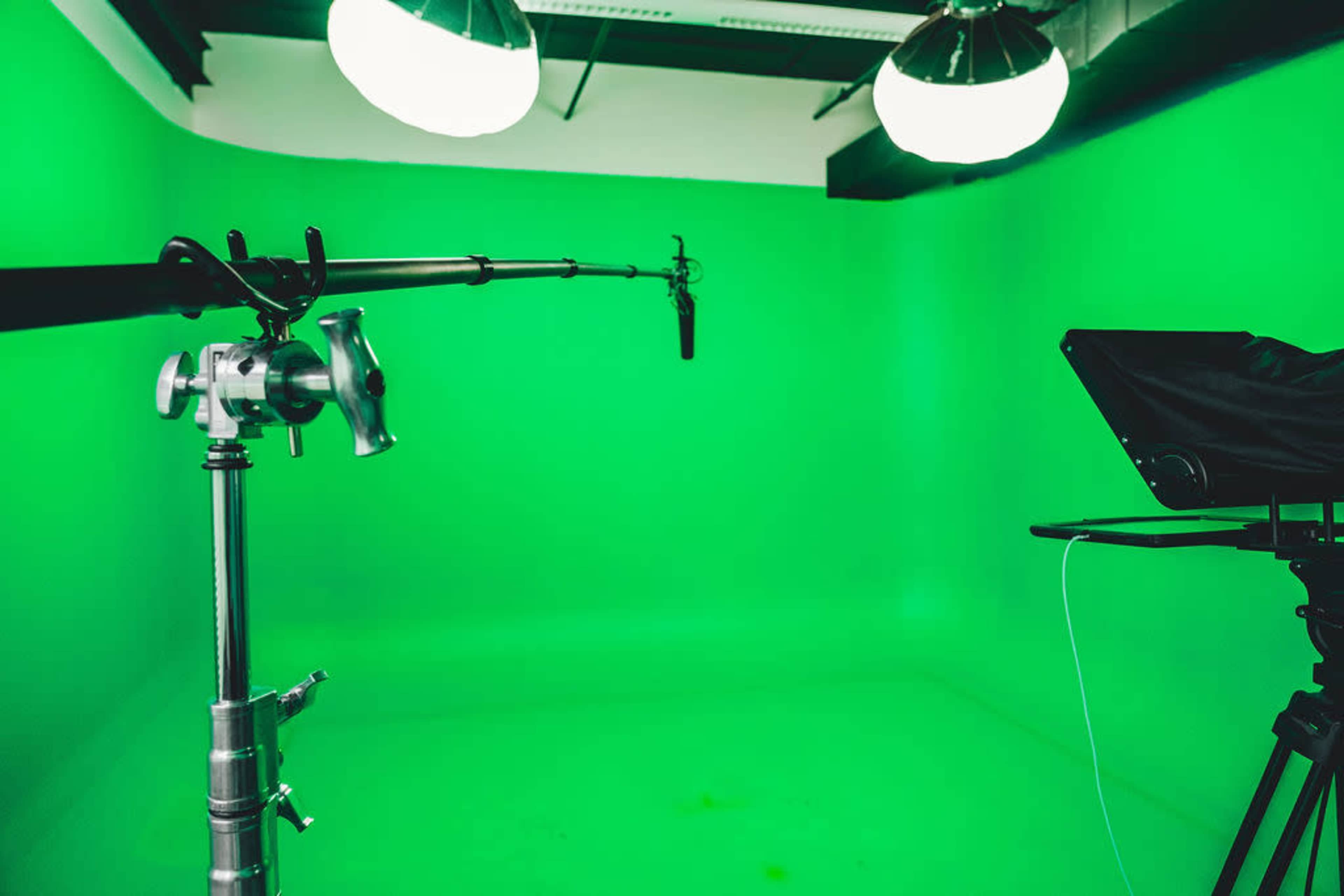 A green screen studio equipped with a microphone on a boom arm and a camera setup.