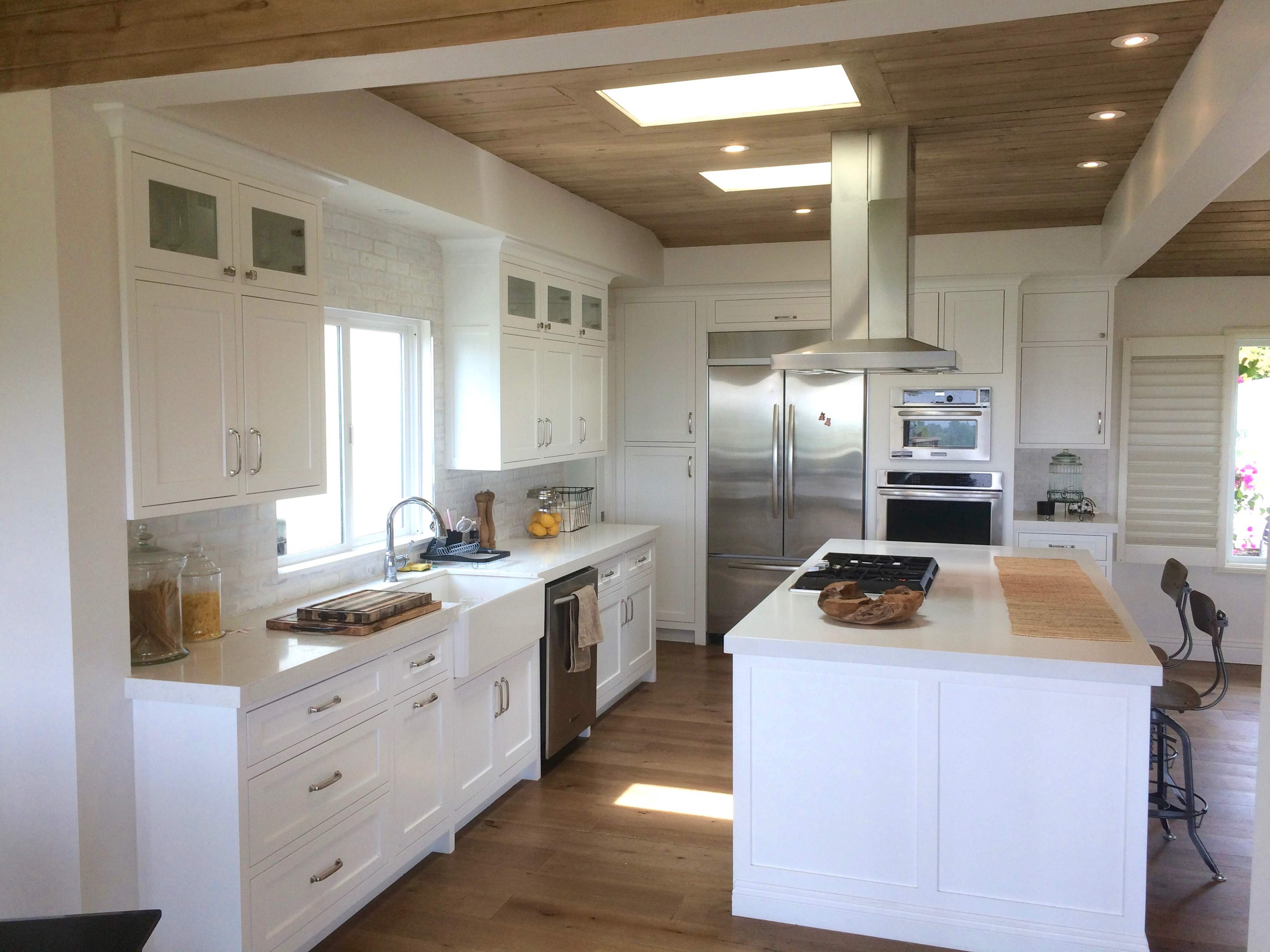 The image shows a modern kitchen featuring white cabinetry, stainless steel appliances, and a large island with a stovetop.