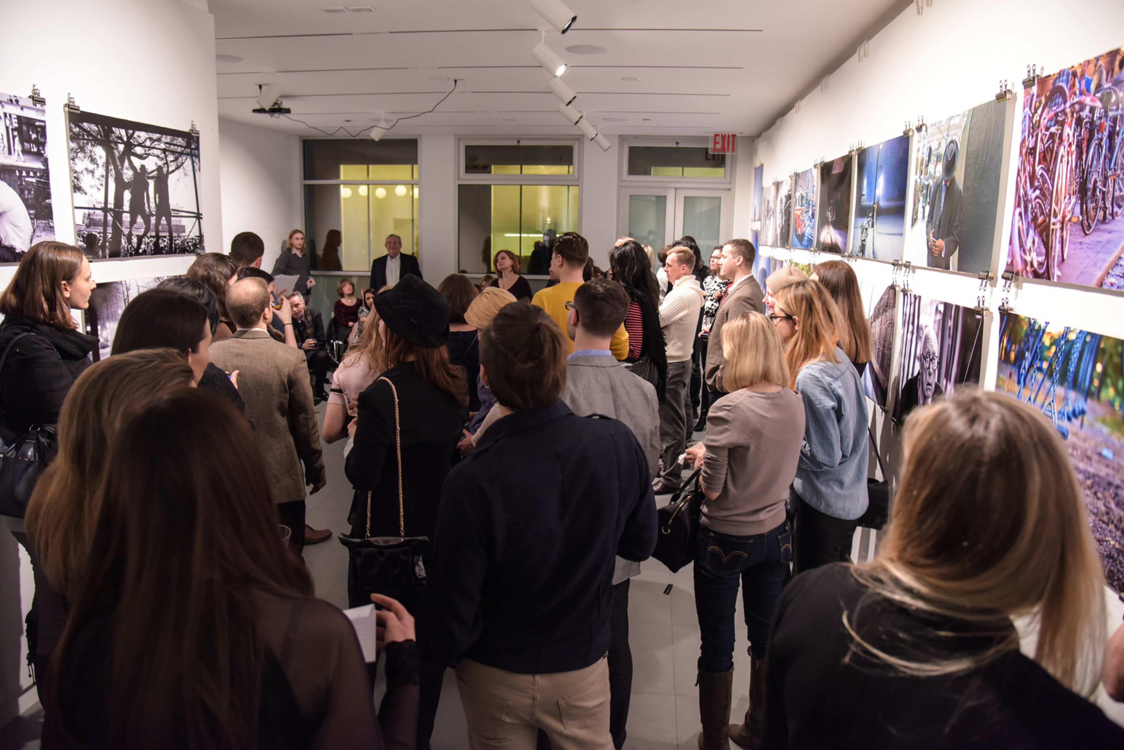 A crowd of people gathers in an art gallery, viewing photographs displayed on the walls.