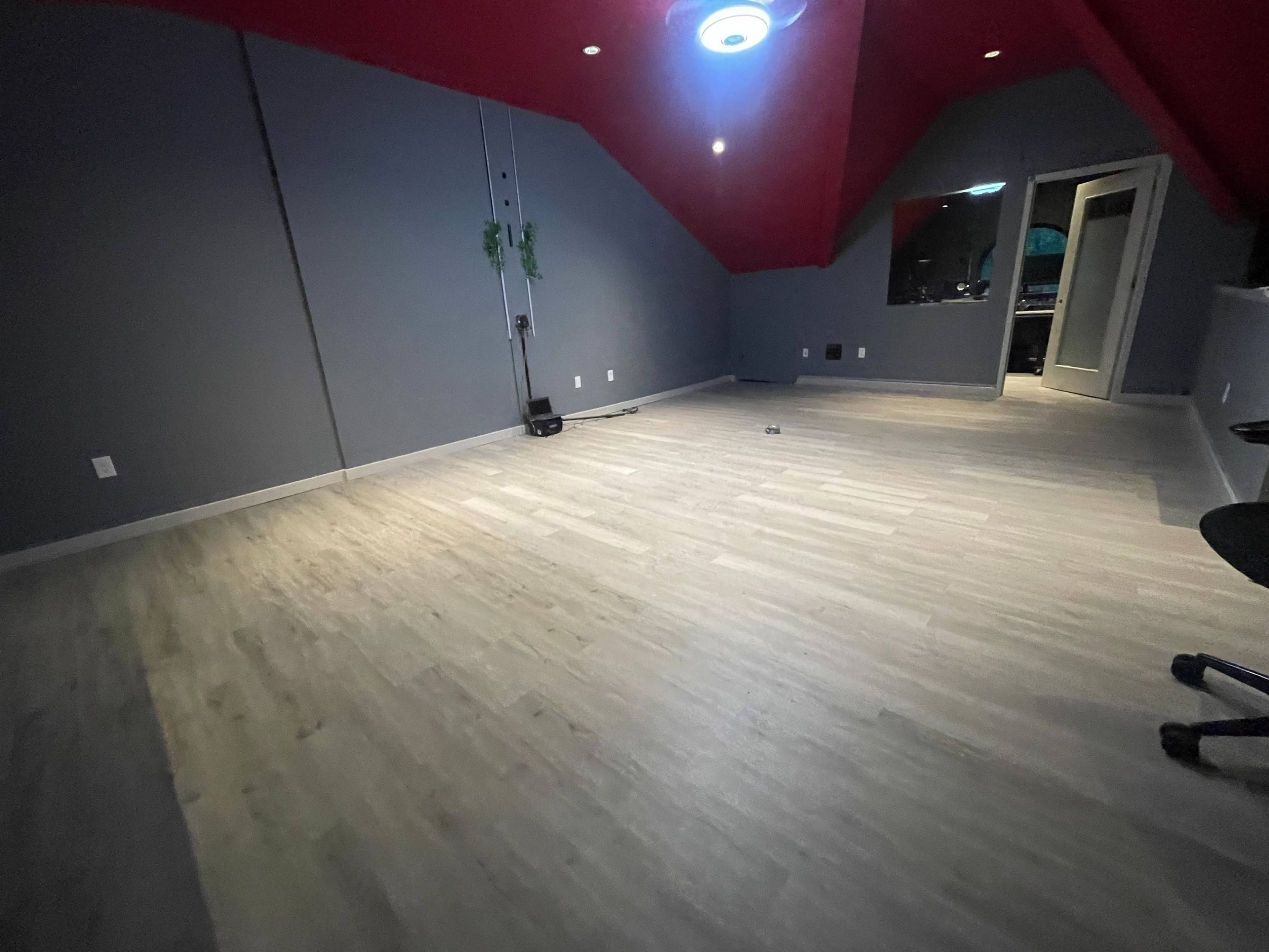 A sparse room with gray walls, red ceiling, and light-colored flooring, featuring a chair in the corner and a door leading to another space.