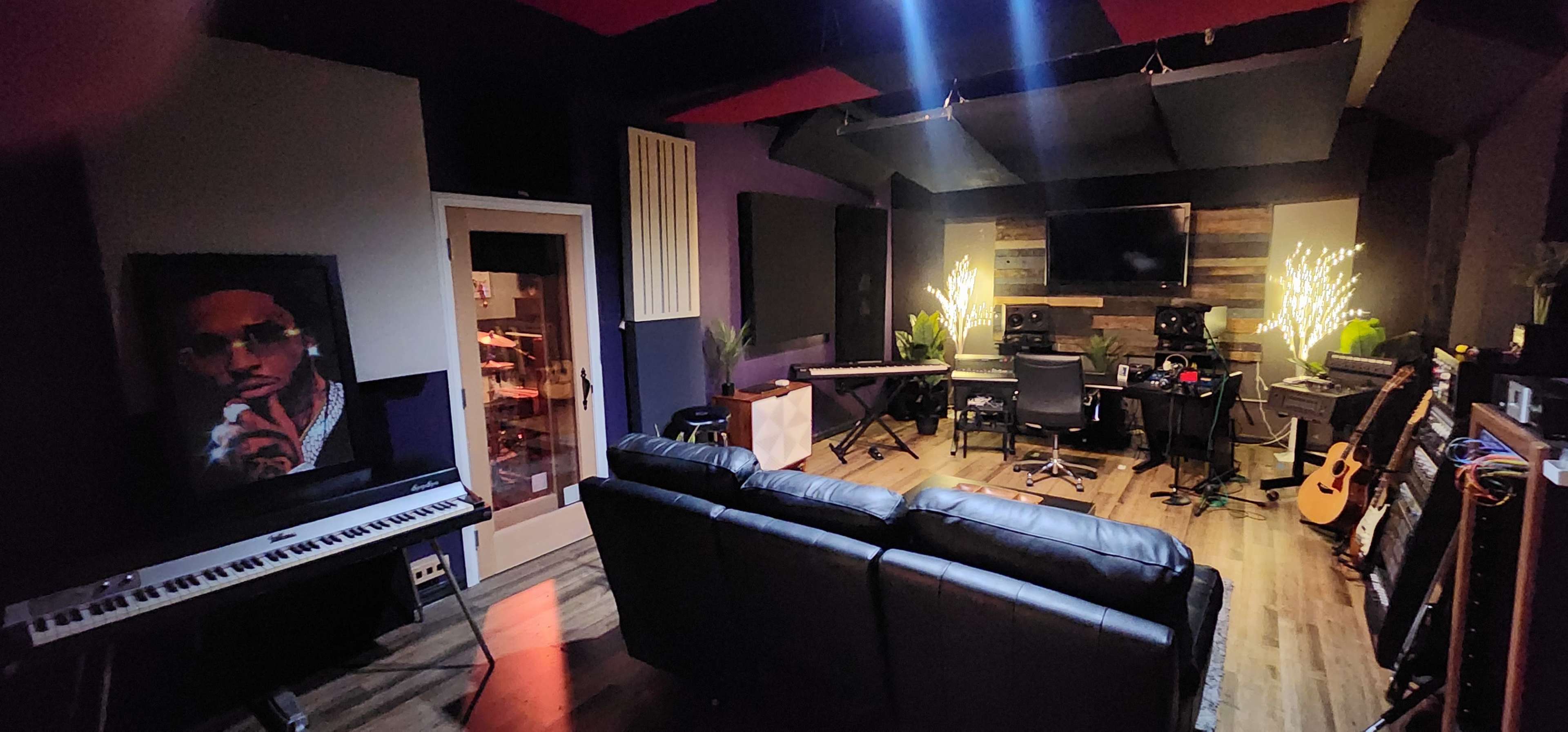 The image shows a music studio with a keyboard, mixing desk, seating area, and various musical instruments displayed around the room.