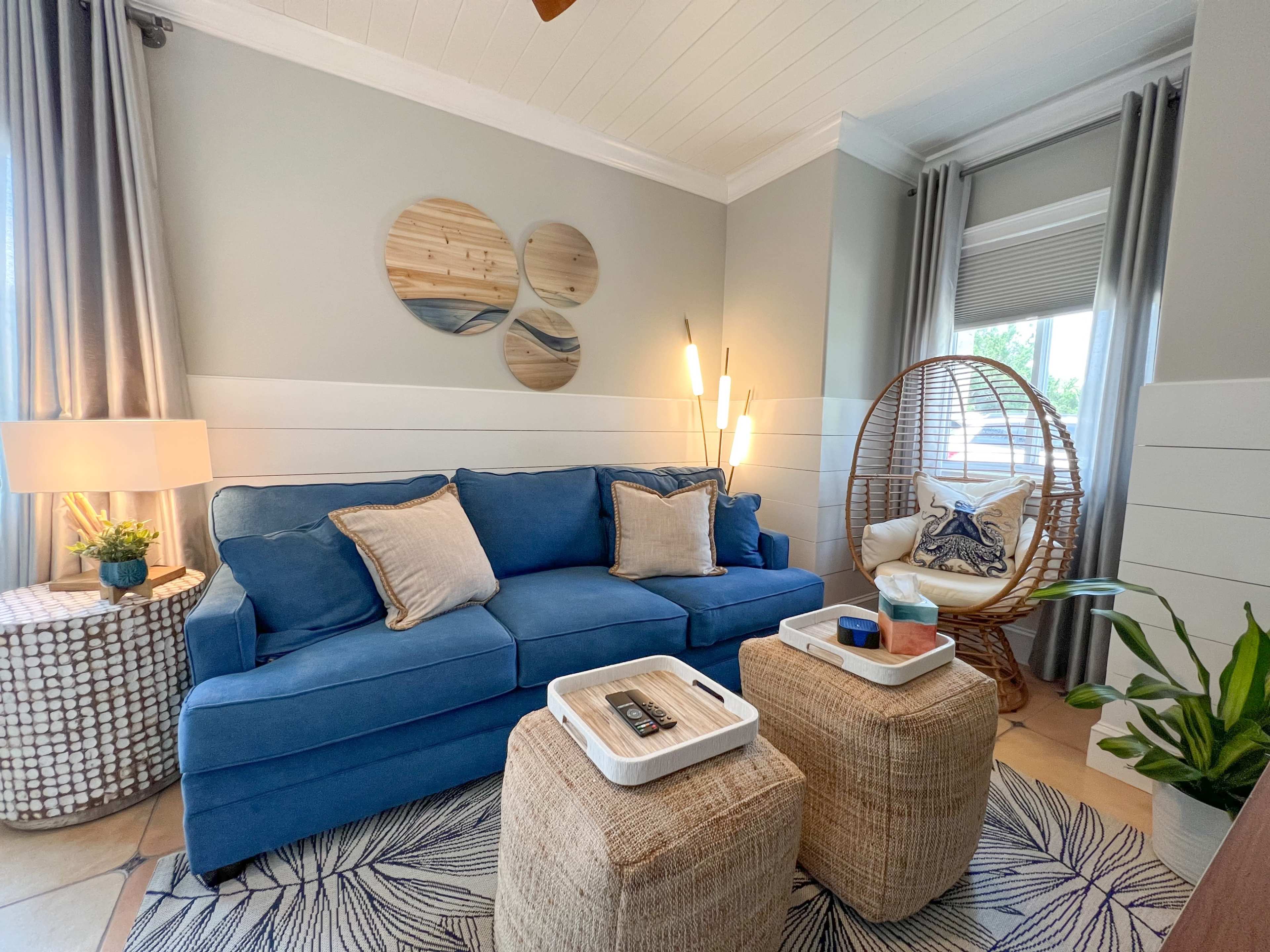 A cozy living room featuring a blue sofa, two wicker side tables, a hanging chair, and decorative wall art.