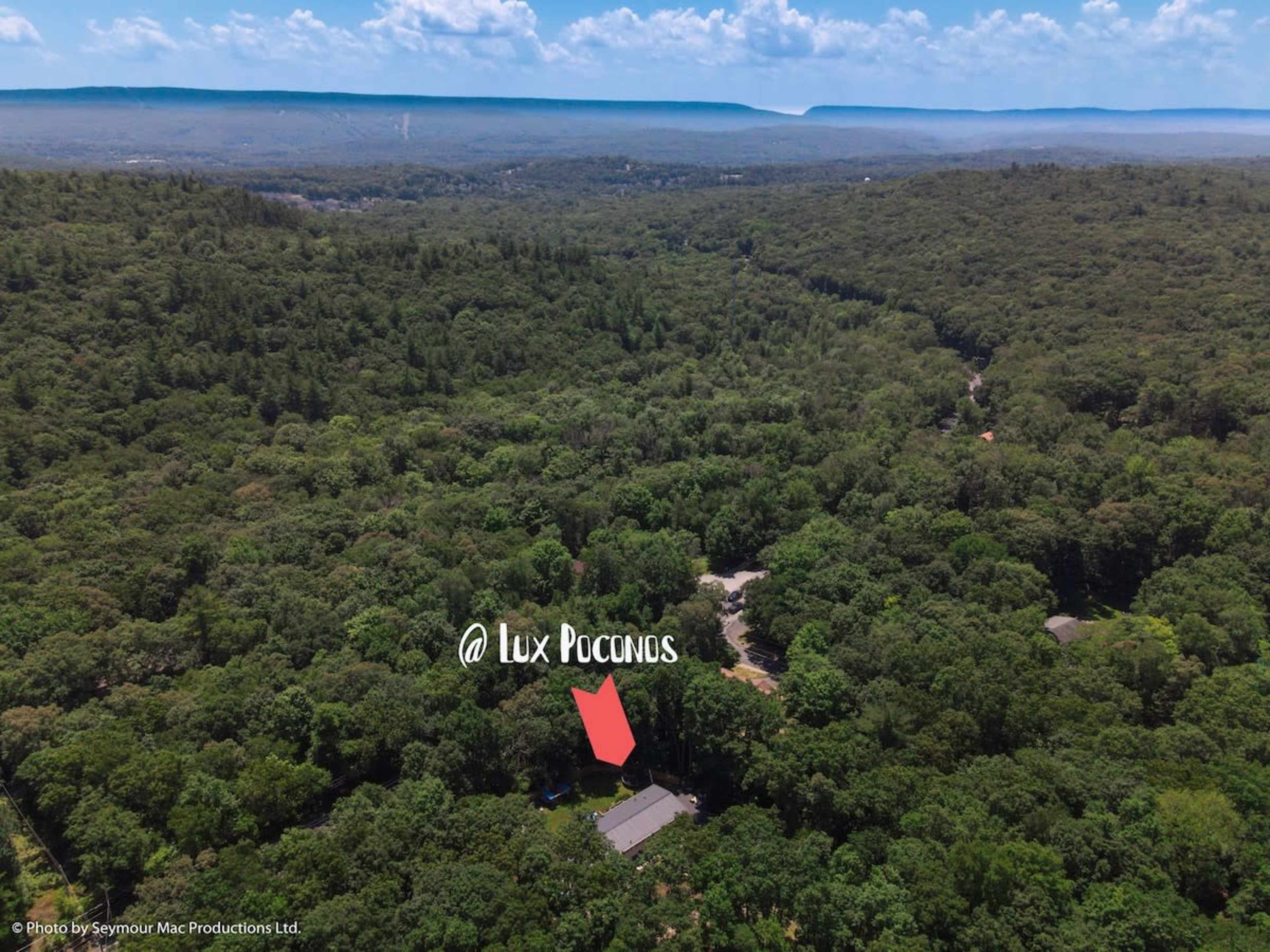 An aerial view shows a single house nestled among dense green forest in the Poconos region.