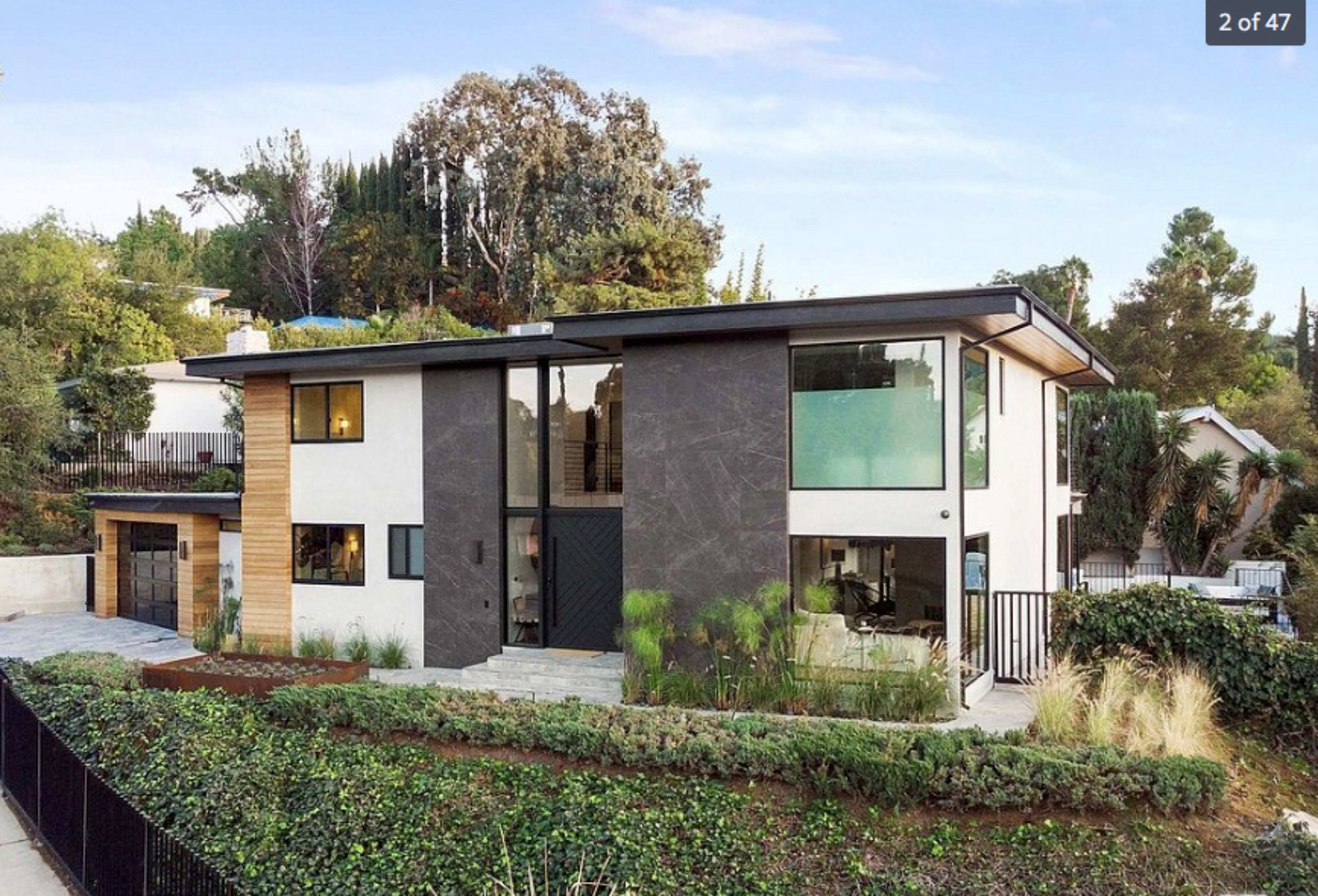 A modern two-story house with distinct black and white exterior walls, large windows, and a landscaped front yard surrounded by a boundary fence.