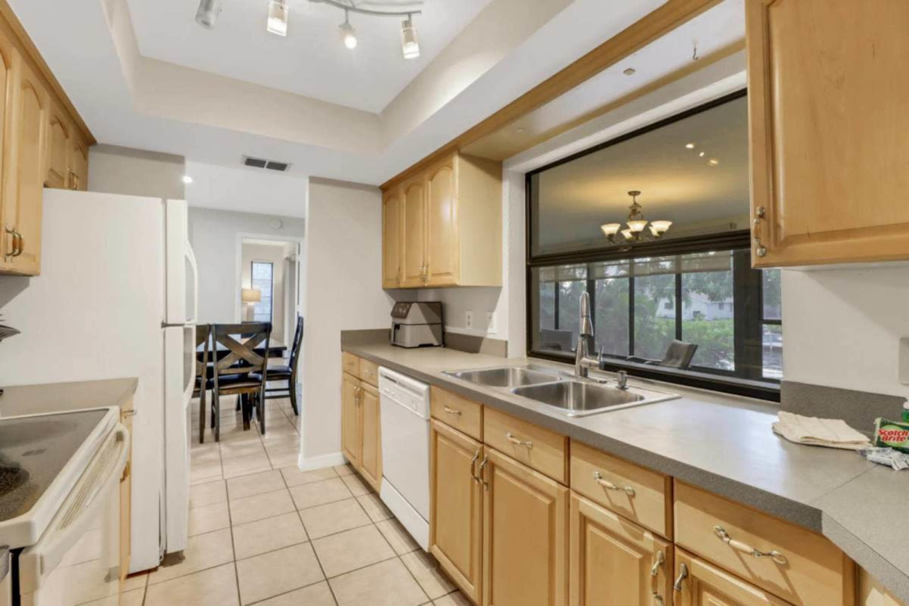 A kitchen with wooden cabinetry, a double sink, and a view of a dining area through a large window.