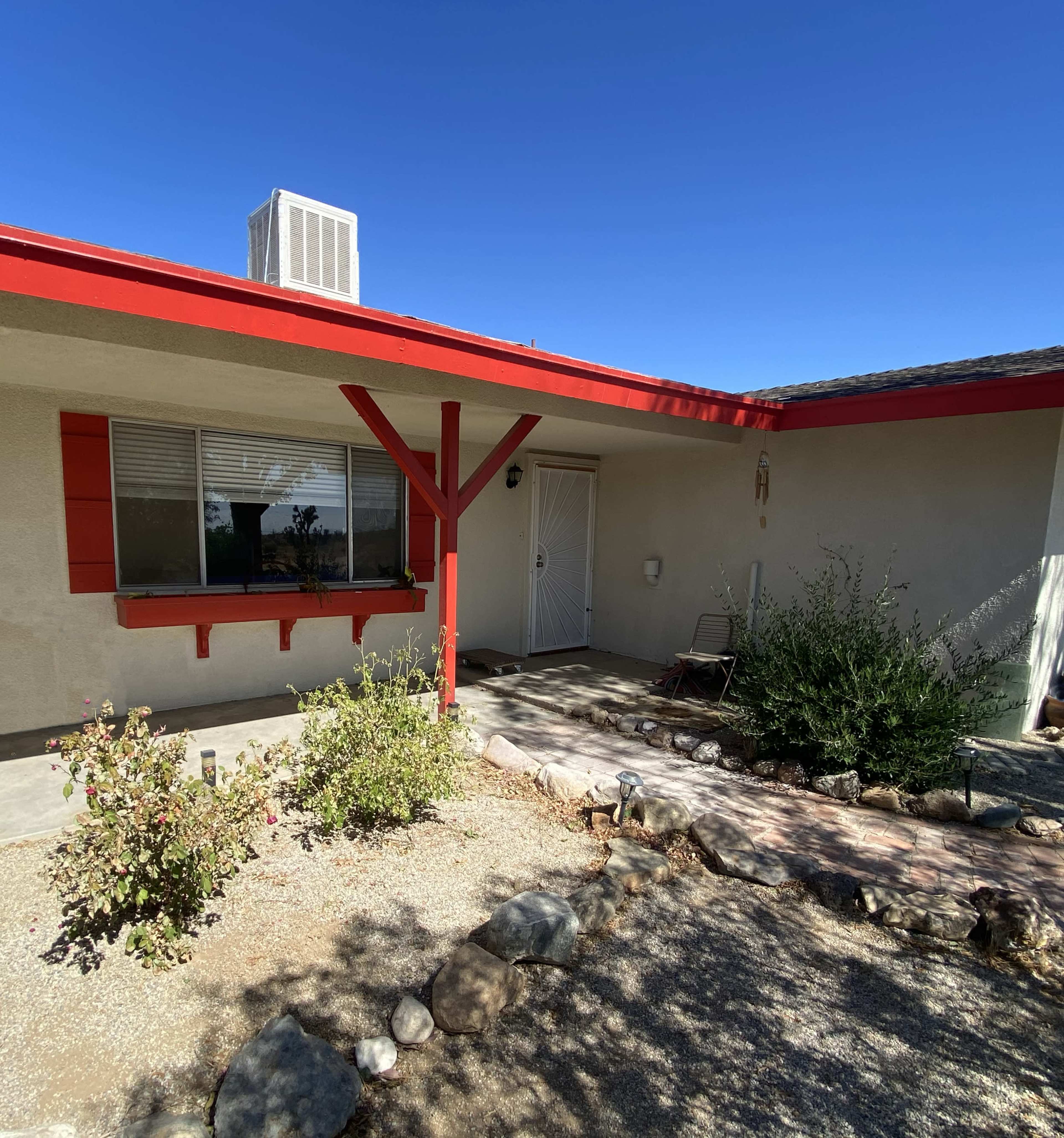 A single-story house with a red accent trim and a neatly landscaped front yard featuring a rock border and desert plants.