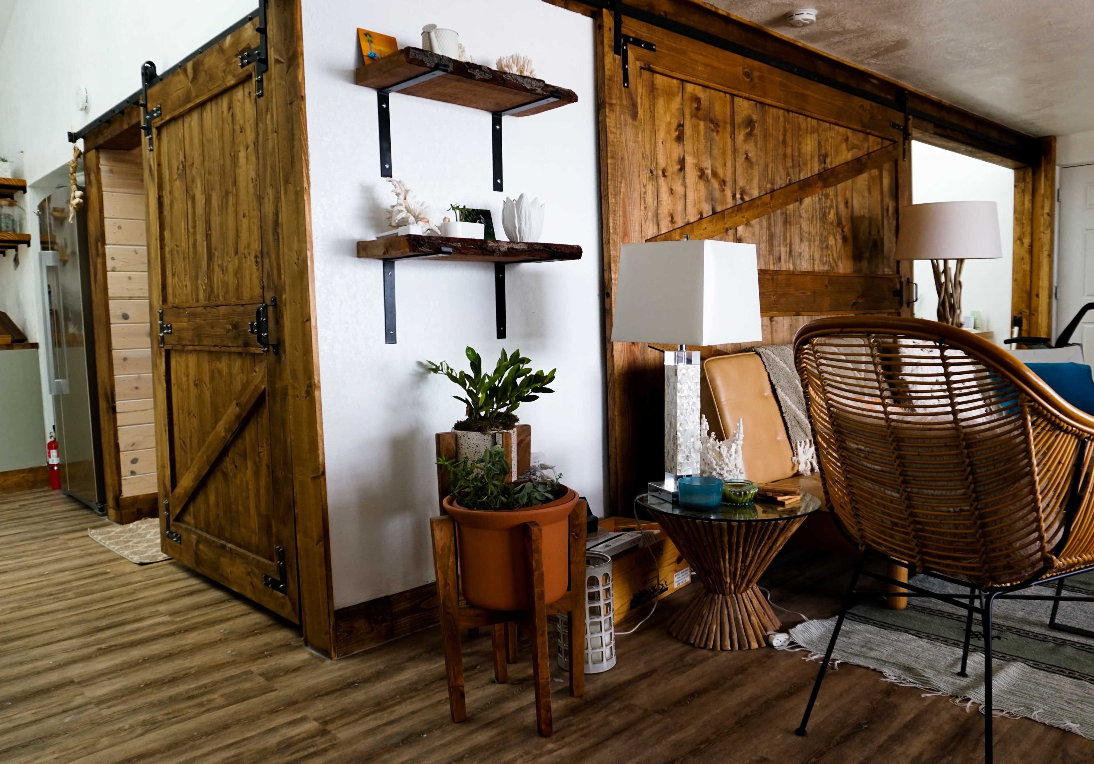 A cozy interior featuring wooden sliding doors, shelves with decor, a potted plant, and a seating area with a rattan chair and side table.